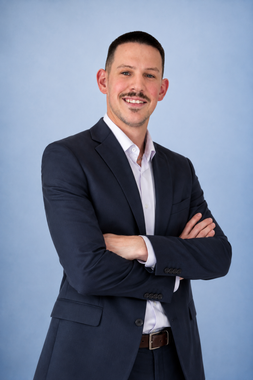 Portrait of a smiling man in a navy blazer and white shirt against a light gray background