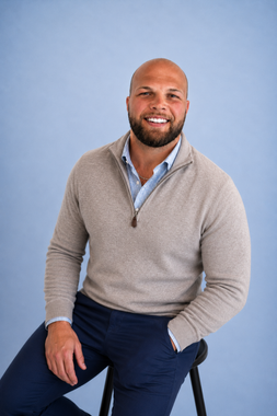 Smiling man in a navy blazer and light blue shirt seated against a light blue background