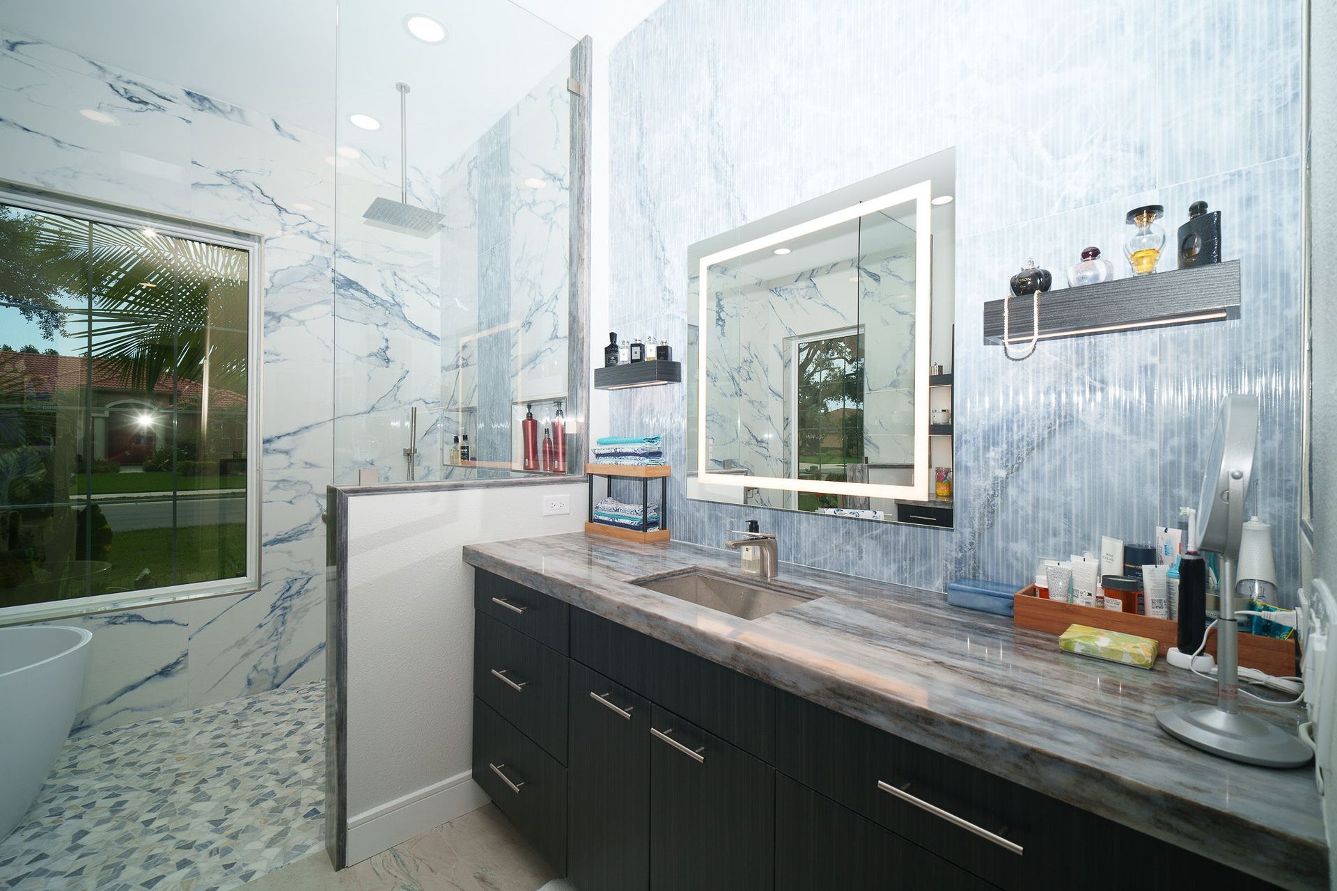 Modern bathroom vanity with dark cabinets, marble walls, mirror, and glass shower door.