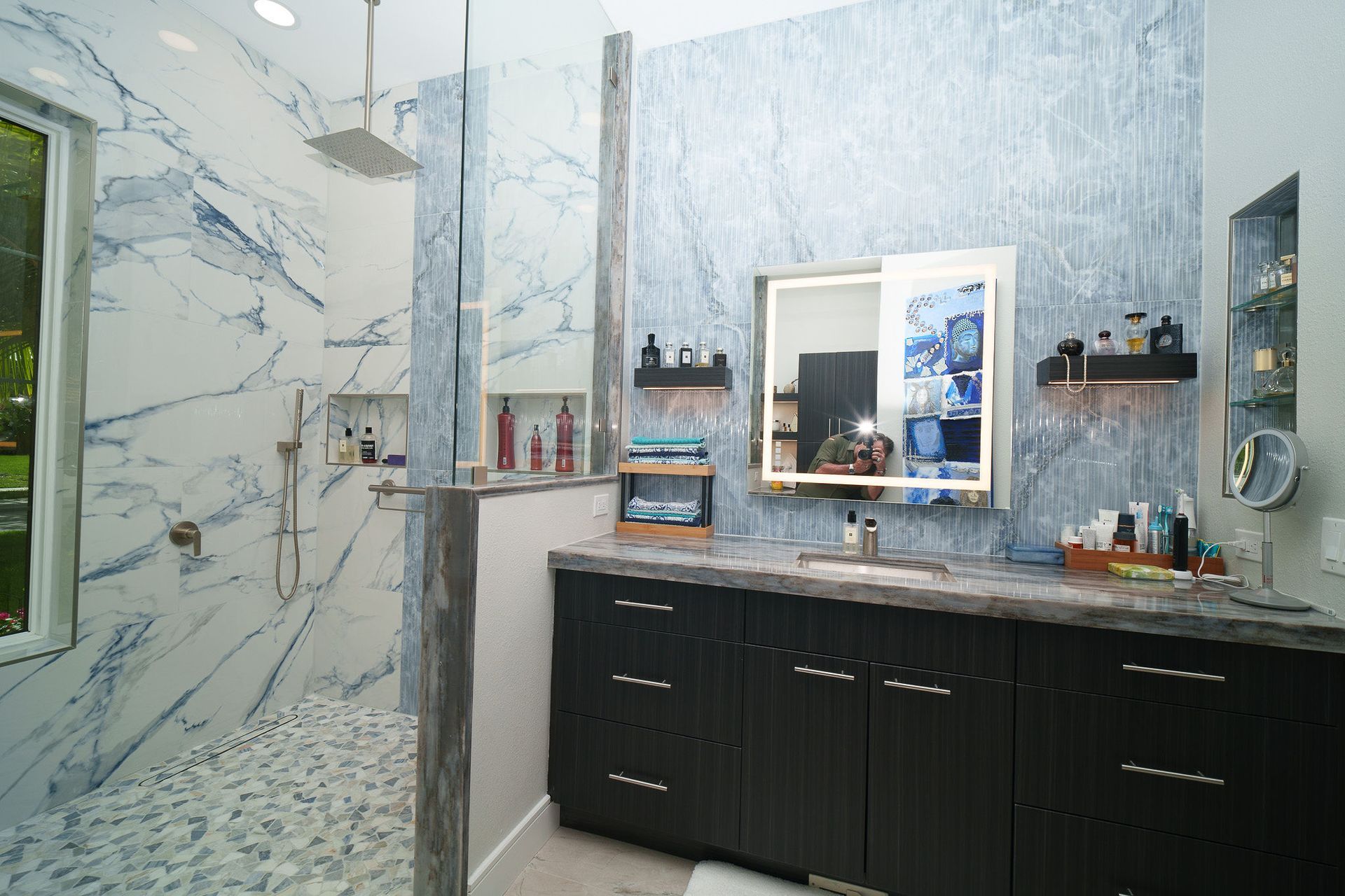 Modern bathroom with marble walls, black vanity, double sinks, and large mirror.