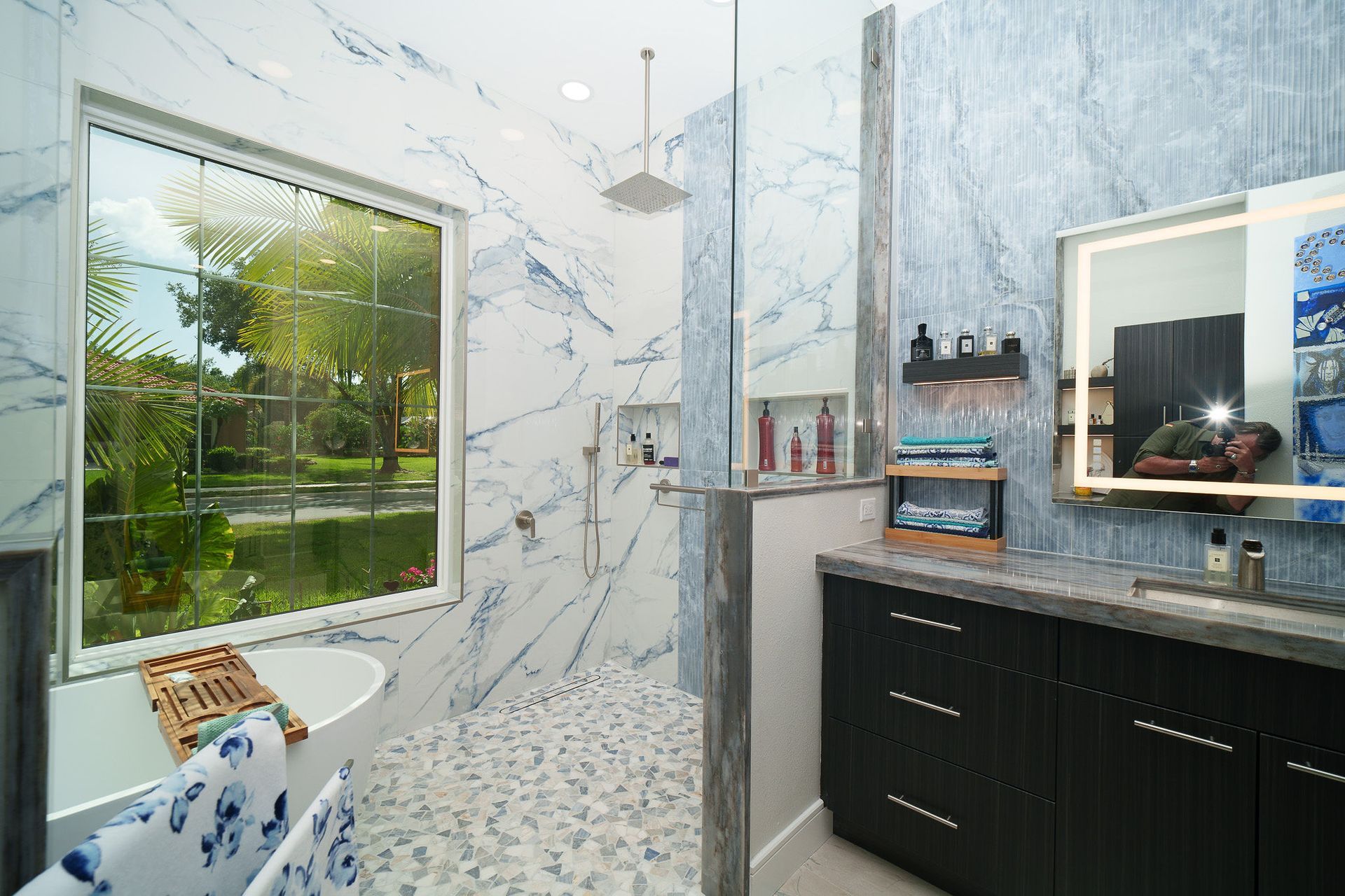 Bright modern bathroom with marble walls, tiled shower, window, and dark vanity sink.