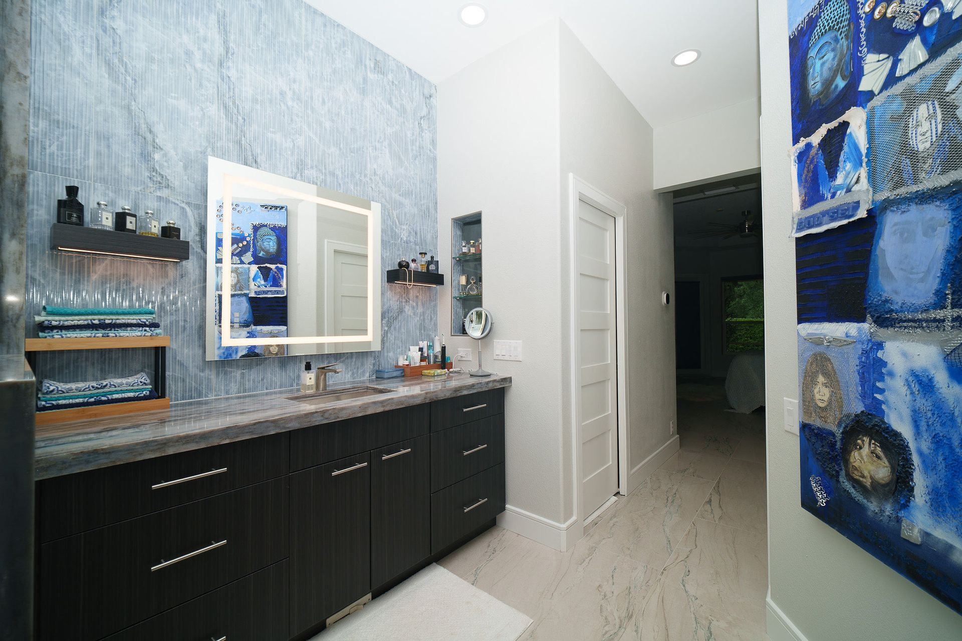 Modern bathroom vanity with dark cabinets, blue decor, mirror, and white hallway door