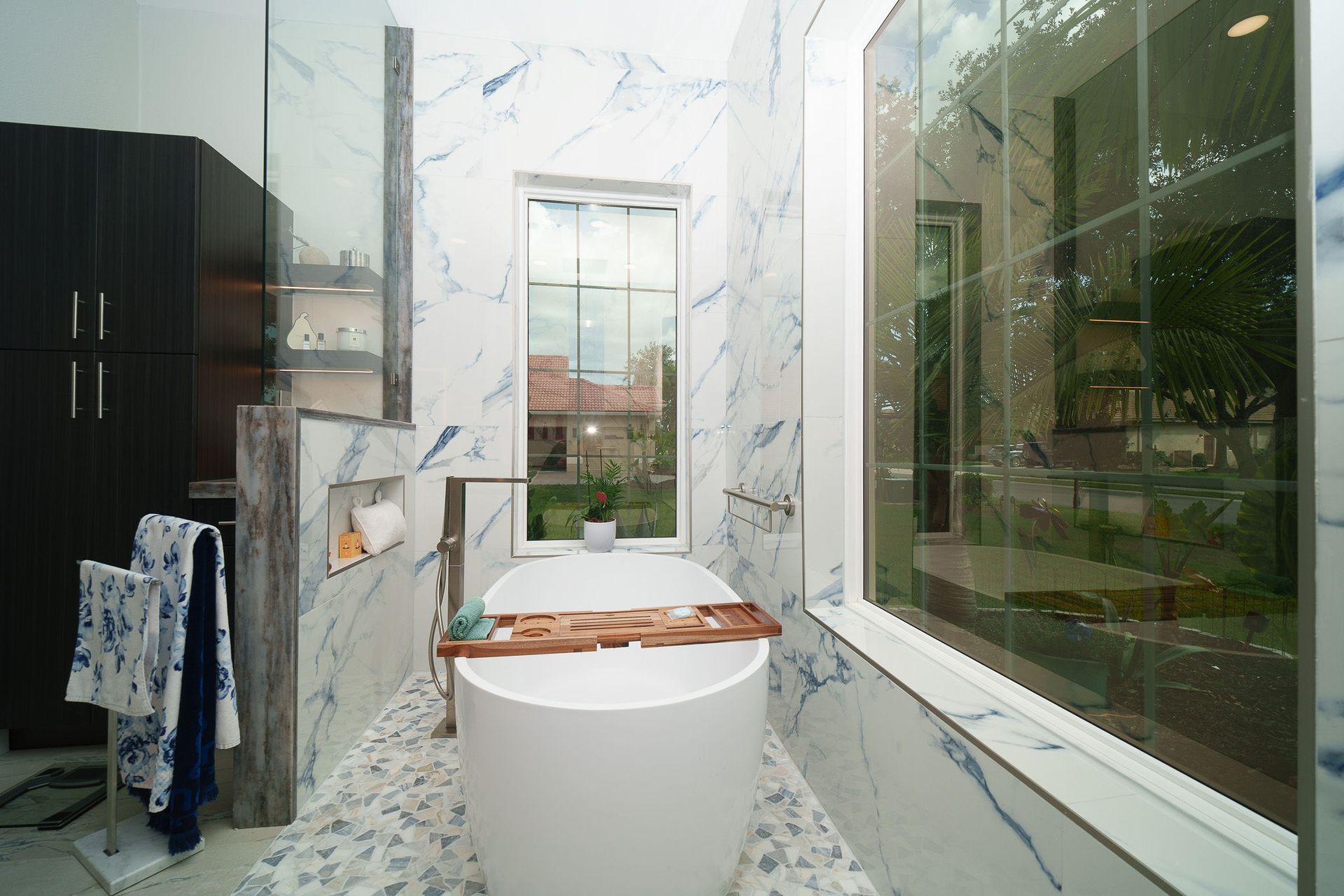 Modern bathroom with freestanding tub, marble walls, and large windows overlooking greenery