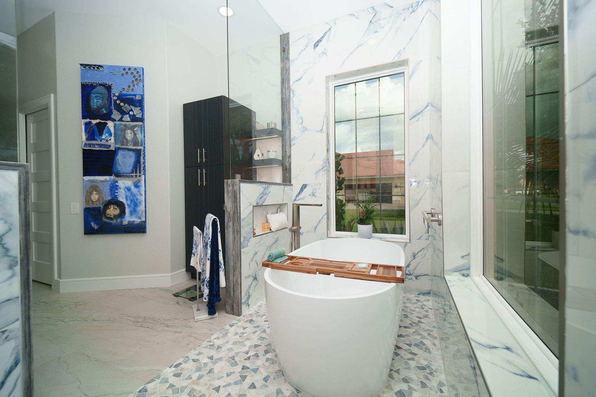 Modern bathroom with marble tile, freestanding tub, glass shower, and dark vanity unit