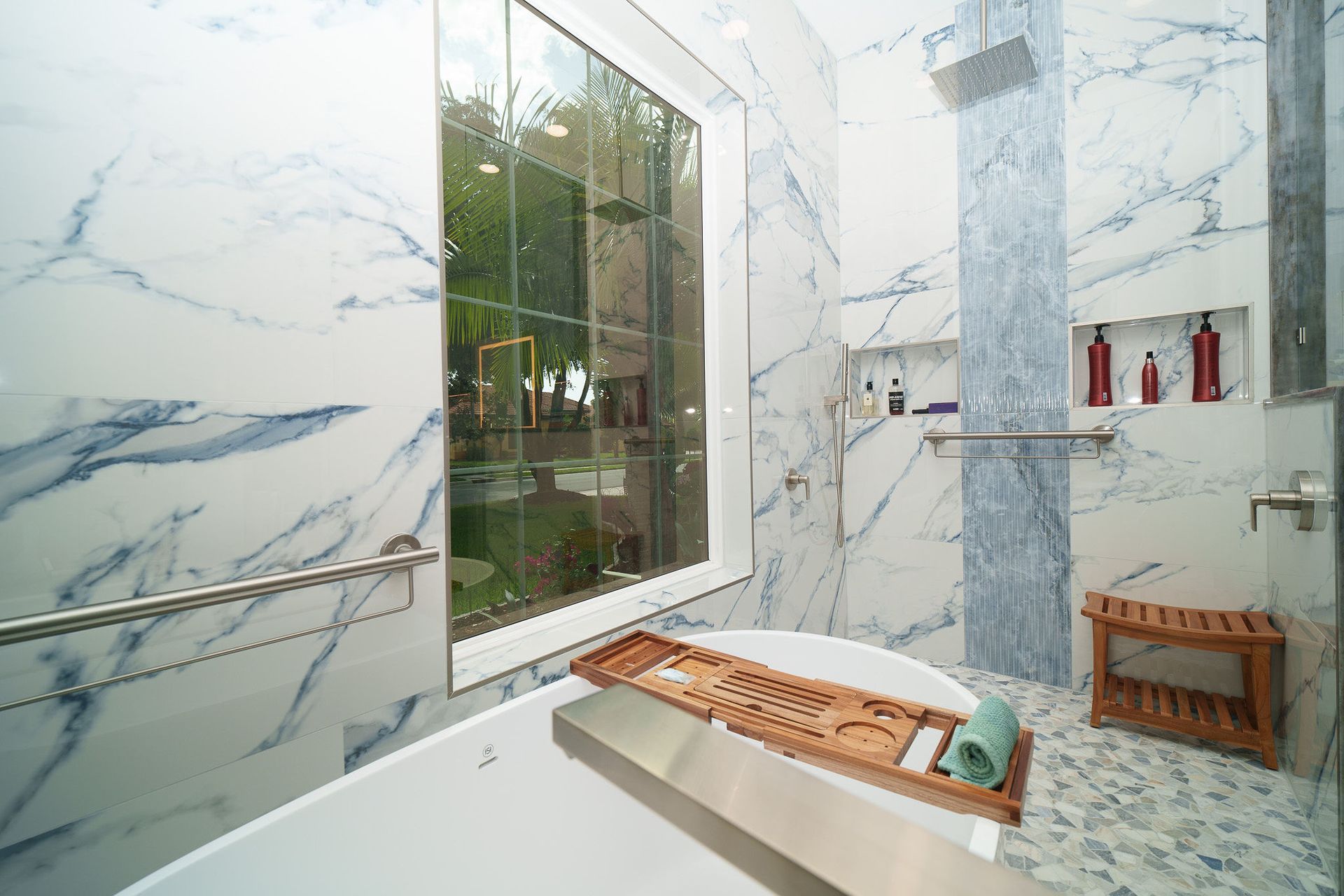Modern bathroom with marble walls, glass shower, and a wooden bench by a window