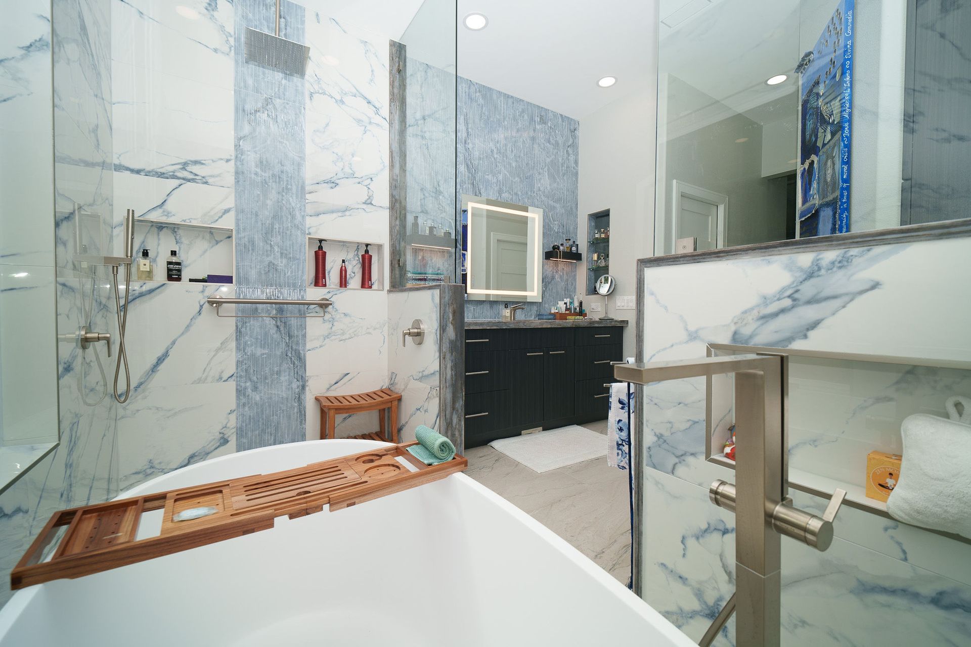 Modern bathroom with marble walls, glass shower, freestanding tub, and vanity mirror