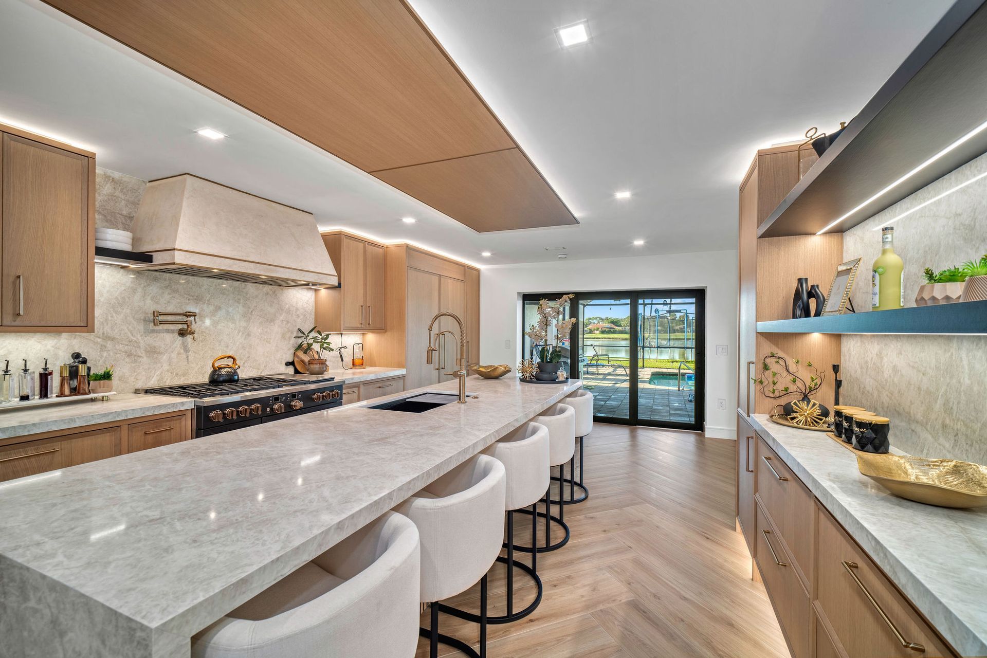 Modern kitchen with white marble island, light wood cabinets, and sliding glass doors to a patio.