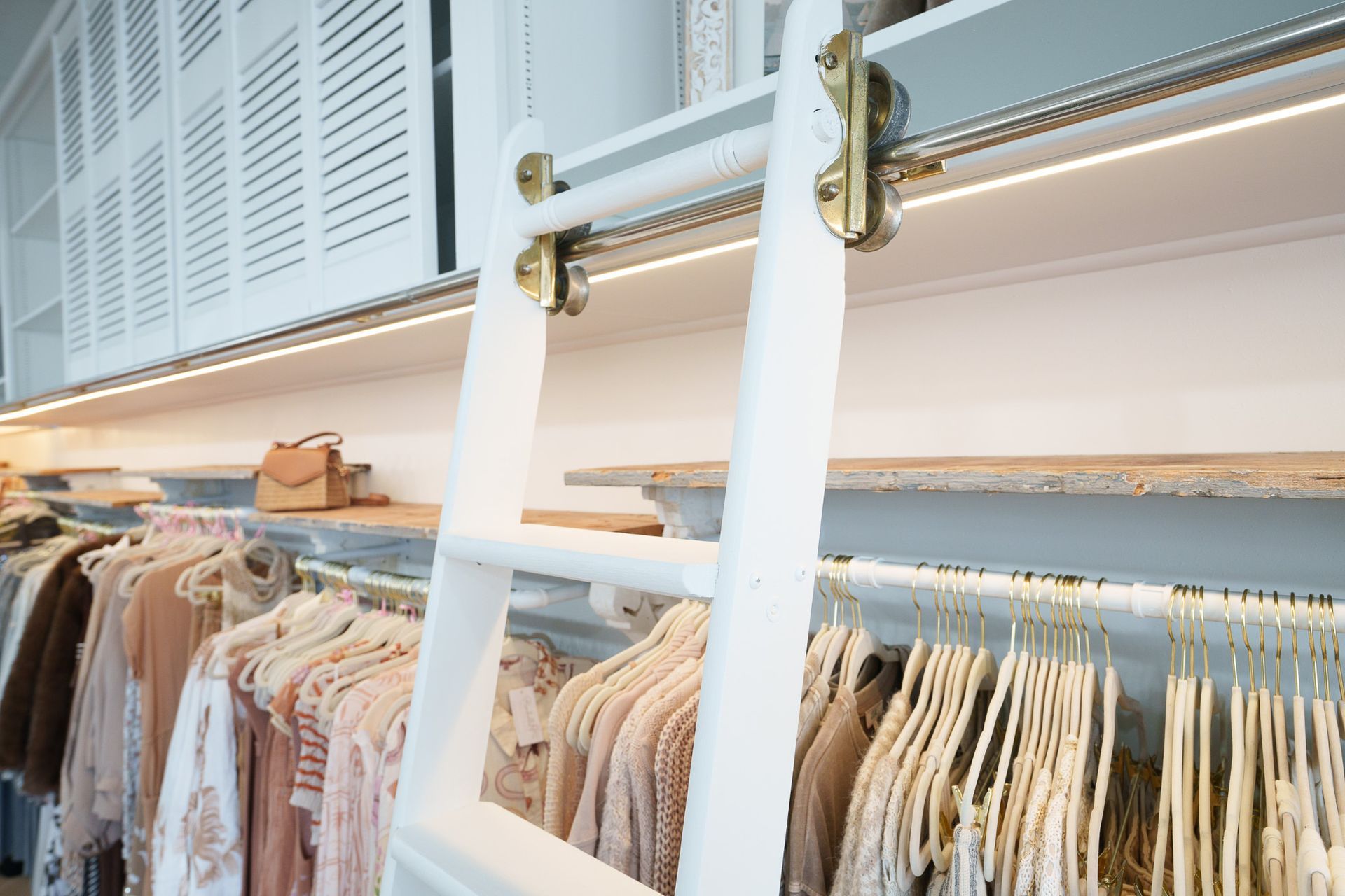 Clothing racks beneath a white loft with a ladder and hanging pastel garments