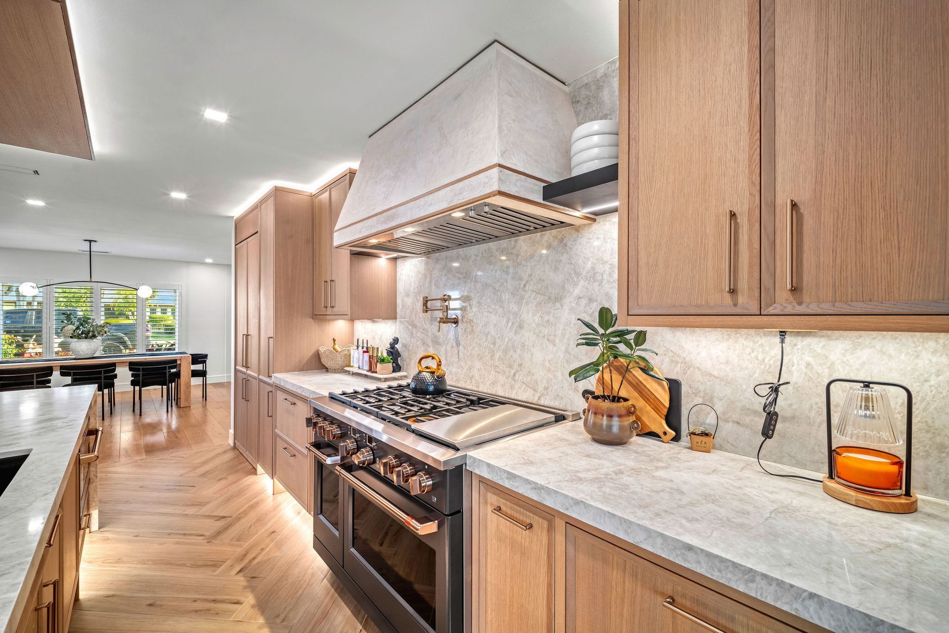Modern kitchen with wood cabinets, marble counters, stainless stove, and bright open layout