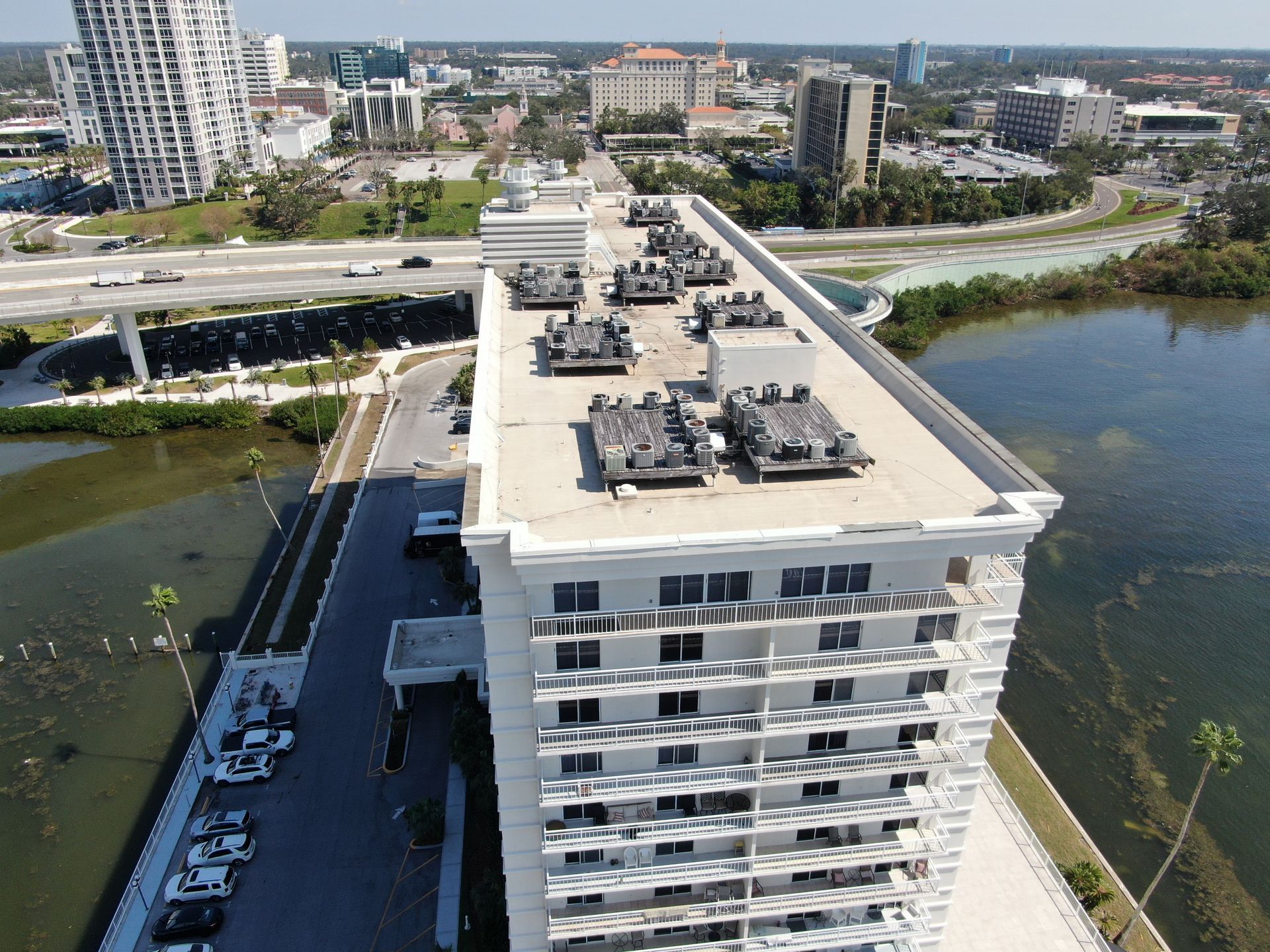 Aerial view of a rooftop pool and white apartment building beside water and a bridge.