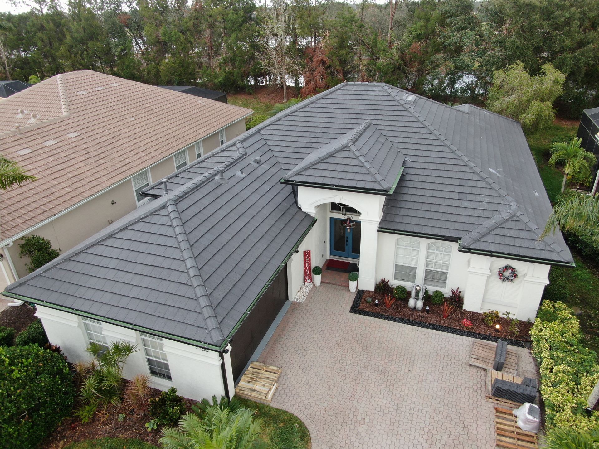 Aerial view of a modern white house with a dark gray roof and a paver driveway.