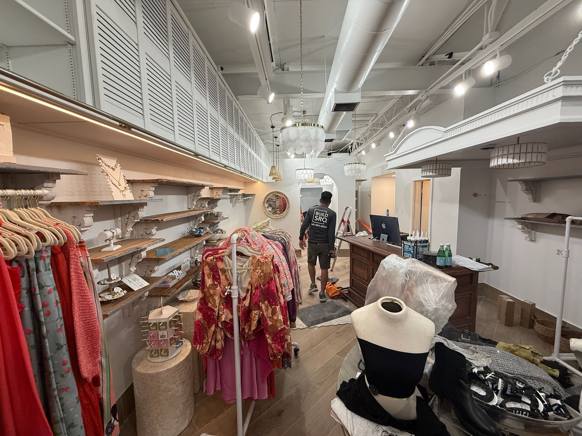 Clothing boutique interior with racks of colorful garments, hats, and shelves under bright ceiling lights.