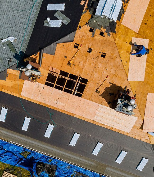 Roof under construction with workers, orange sheathing, and a gray street below.