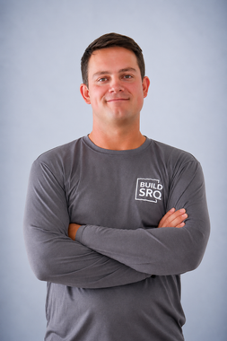 Smiling man in a navy blazer and light blue shirt seated against a light blue background
