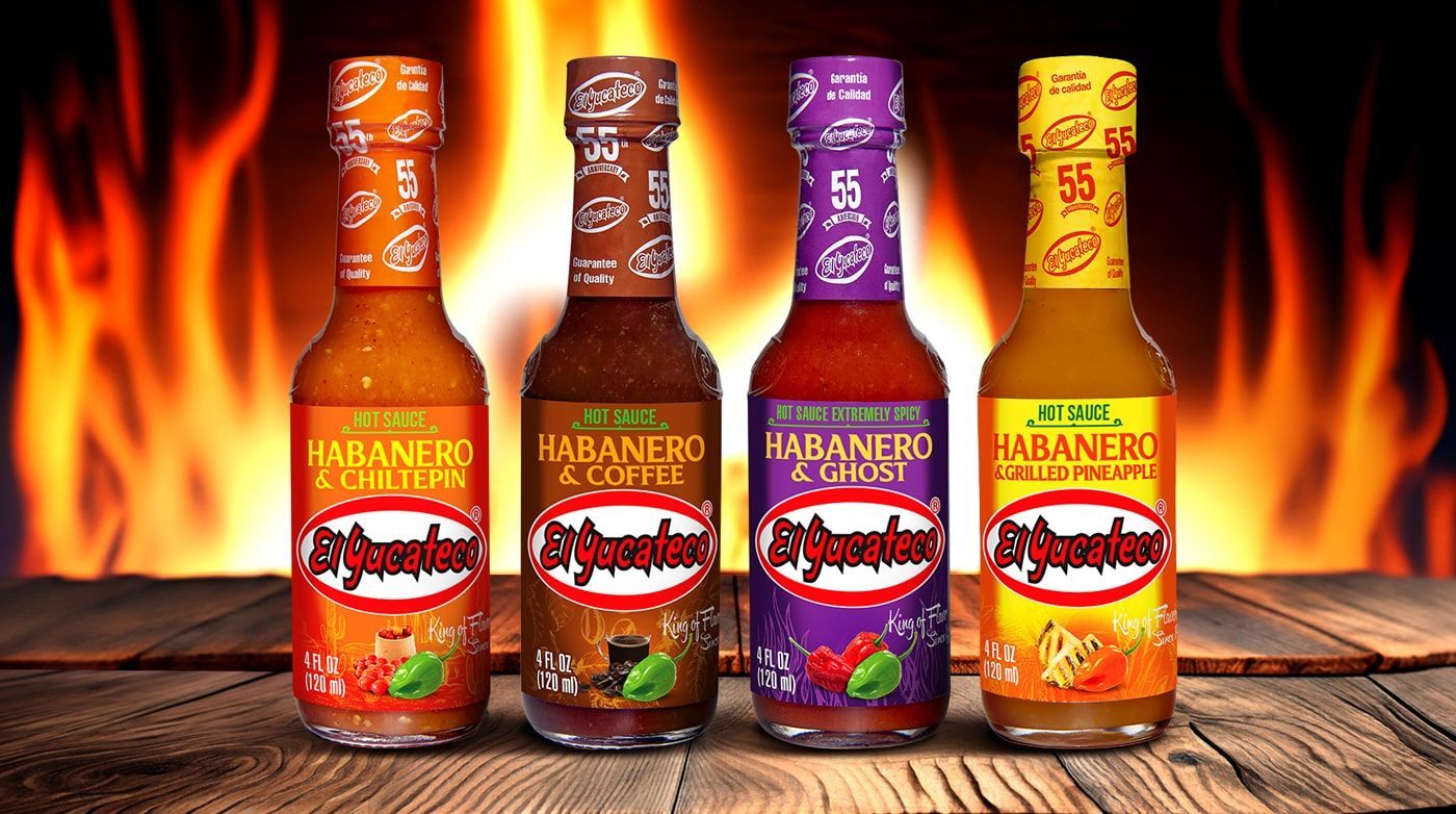 Cuatro botellas de salsa picante con diferentes etiquetas, frente a un fondo de llamas.