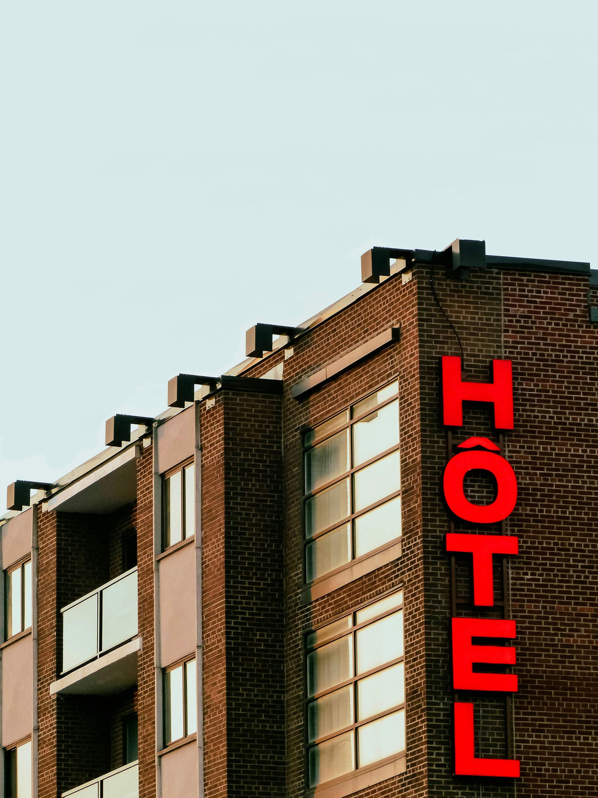 Brick hotel building with a vertical red “HOTEL” sign against a pale sky