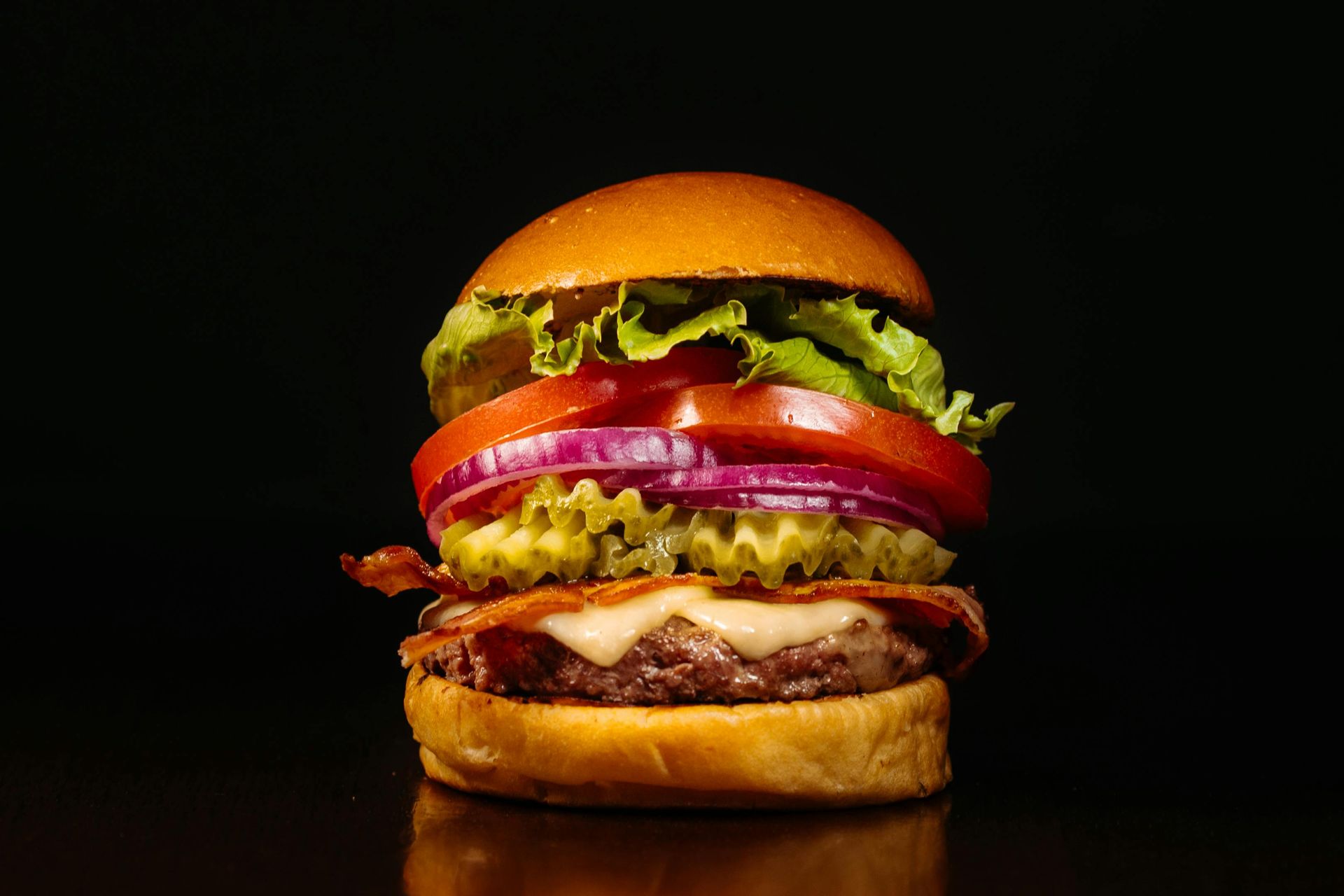 Stacked cheeseburger with tomato, lettuce, onion, pickles, and melted cheese on a black background