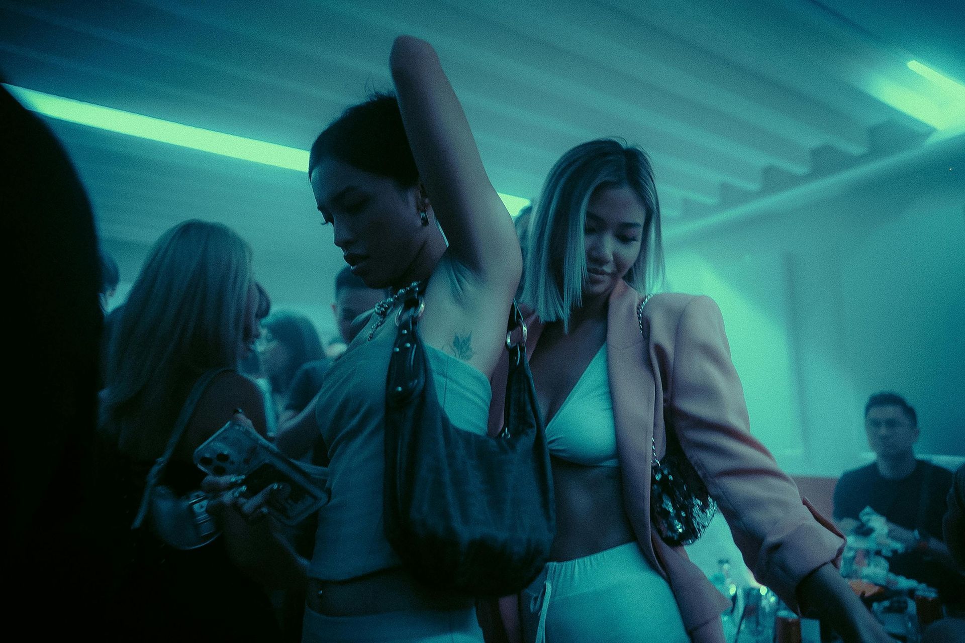 People dancing at a neon-lit club, with blue-green lights and one person holding a drink