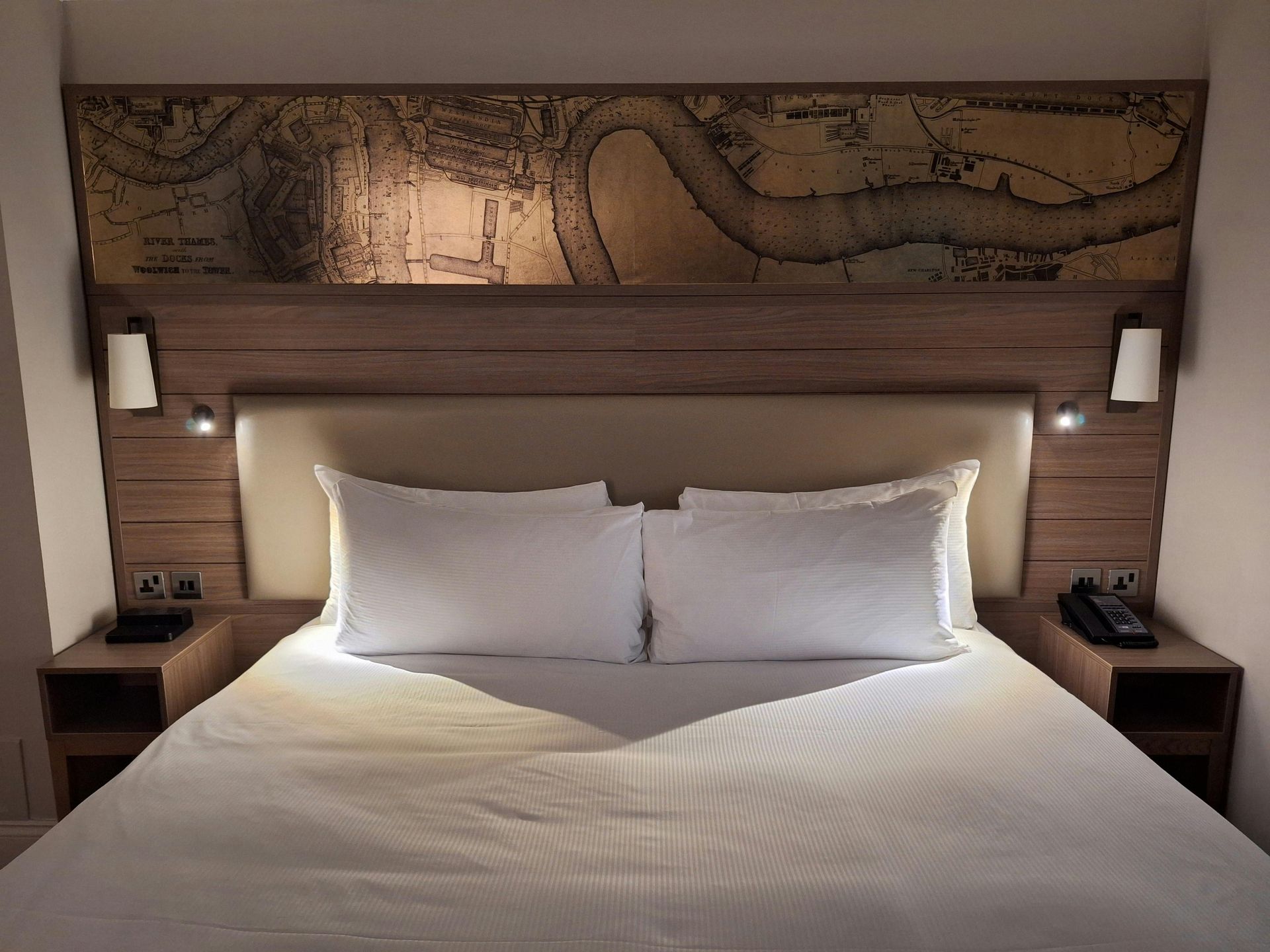 Modern hotel room with a large white bed, warm lighting, and a map mural above the headboard