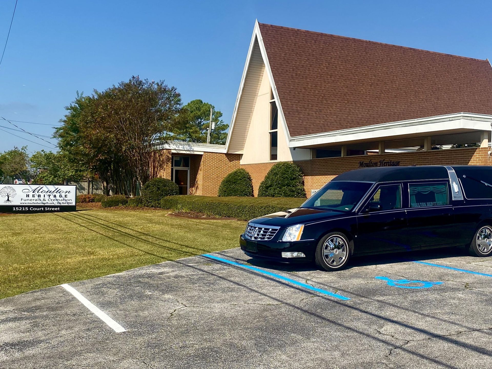 Dark blue minivan parked in a lot beside a church with a steep brown roof and sign.