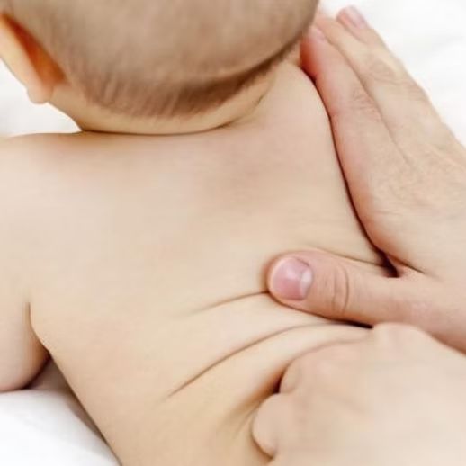 A baby's back is massaged with two hands on a white surface.