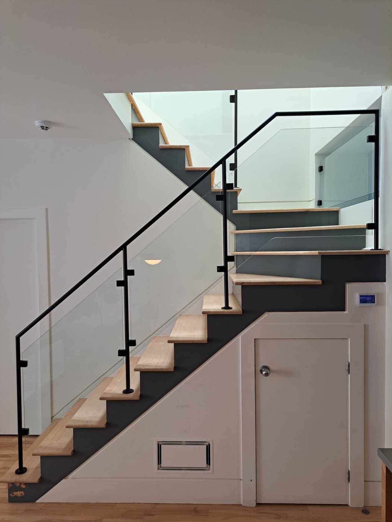 Un escalier avec une rampe en verre et une porte en dessous.