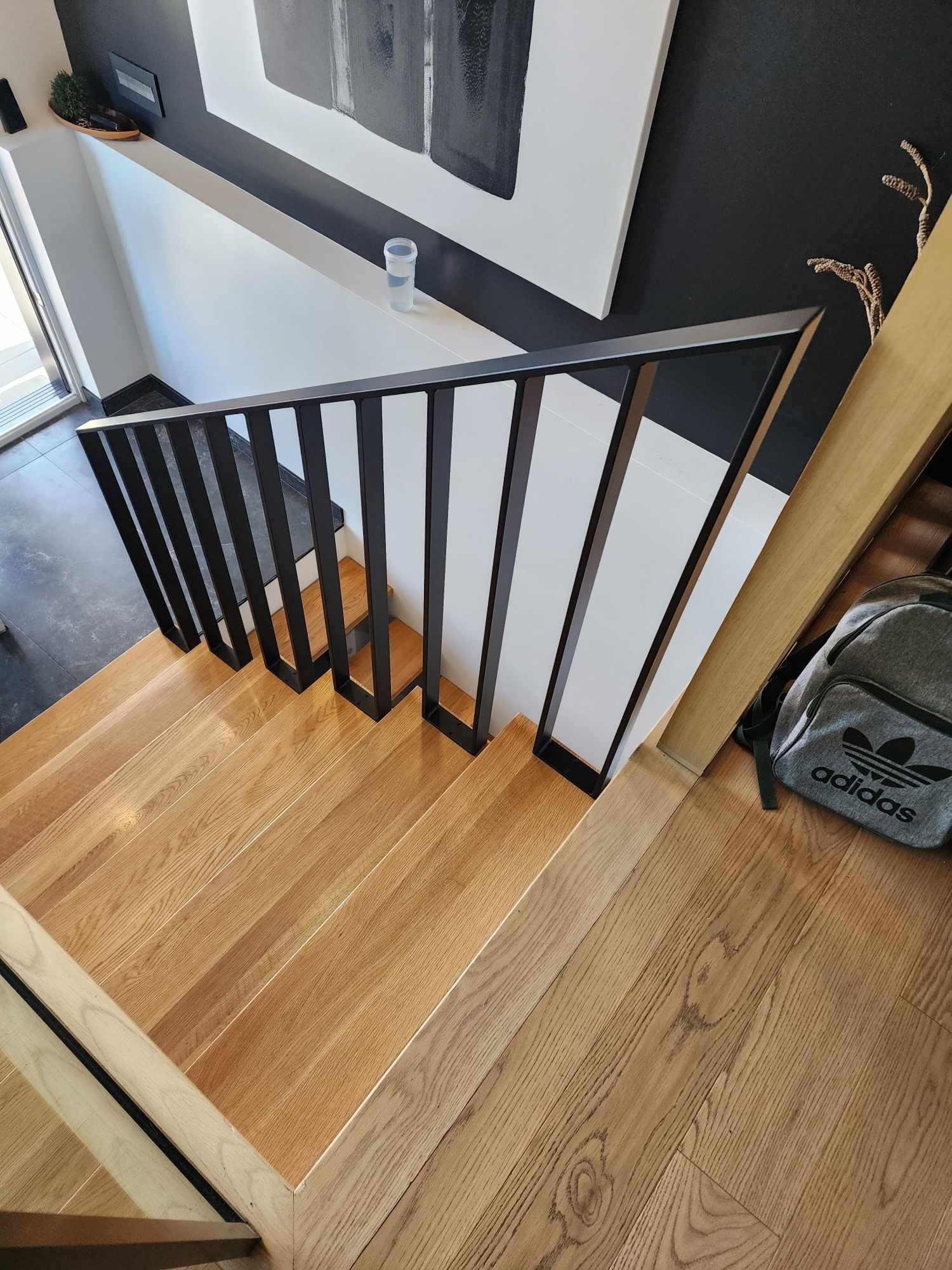 Un escalier en bois avec une rampe en métal et un sac au sol.