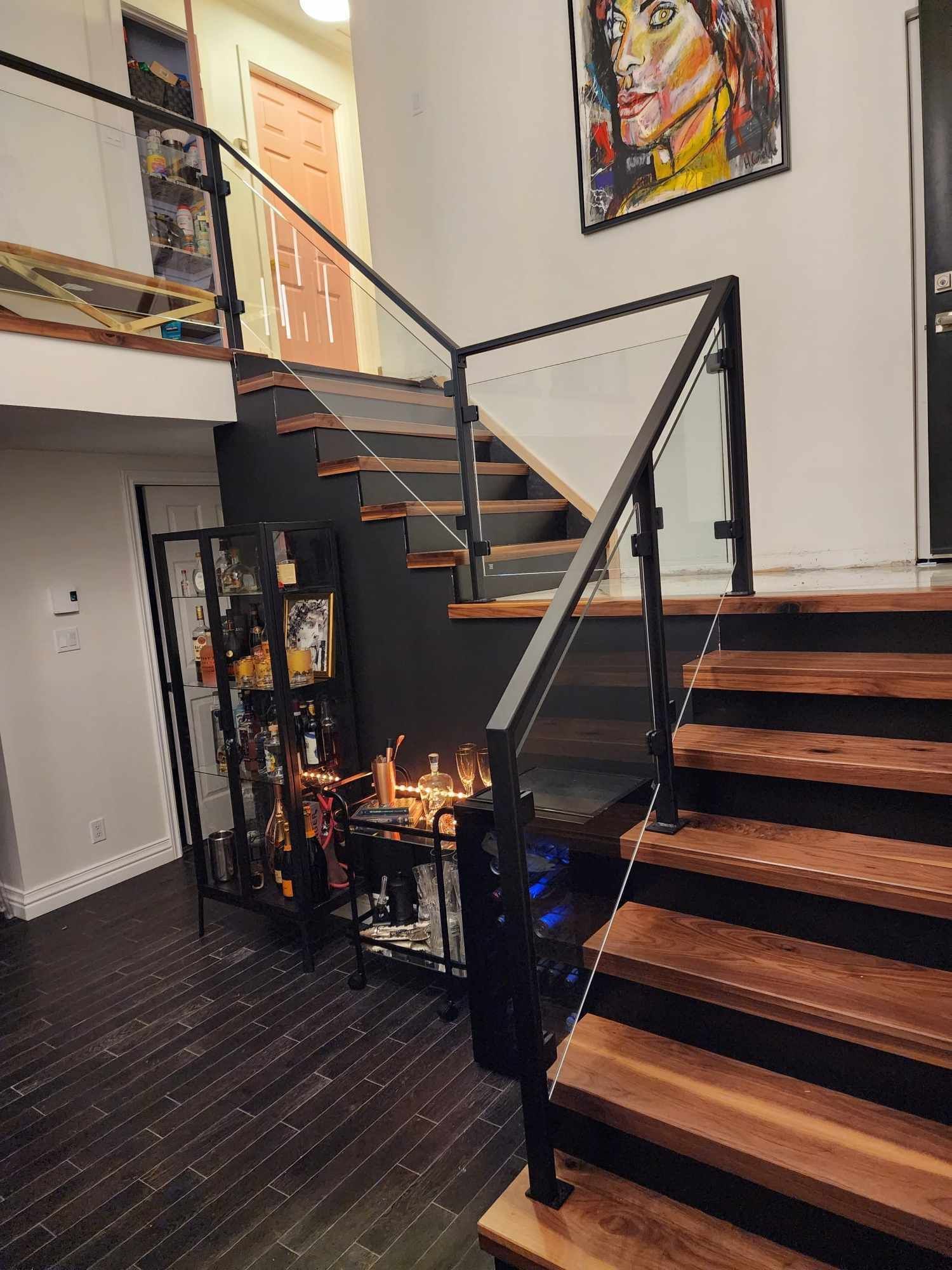 Un escalier en bois avec une rampe en verre et un tableau au mur.