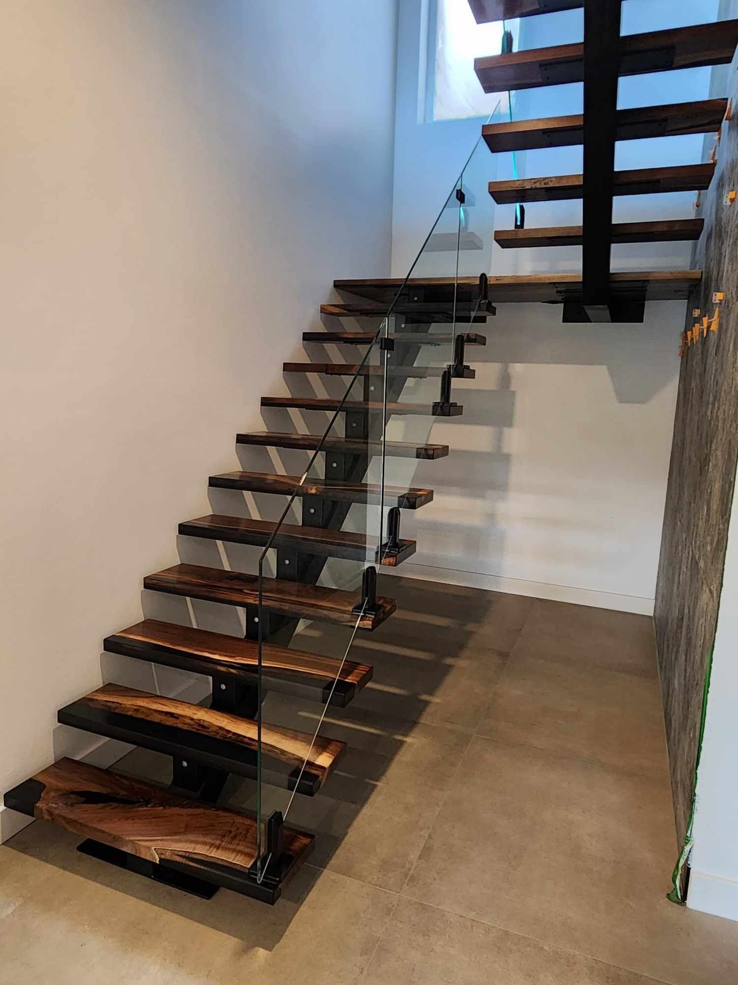 Un escalier en bois avec une rampe en verre dans un couloir.
