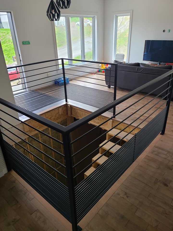 Un salon avec un escalier et une rampe noire.