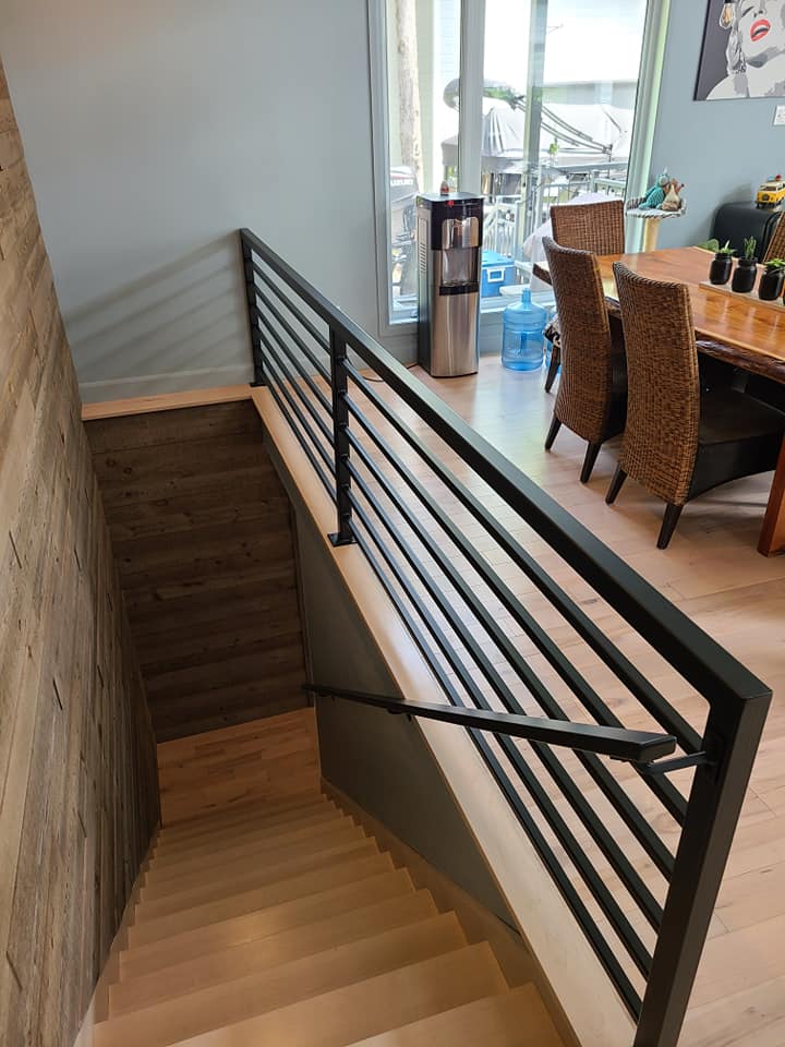 Un escalier en bois avec une rampe en métal menant à une salle à manger.