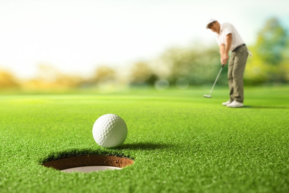 A man is putting a golf ball into a hole on a golf course.