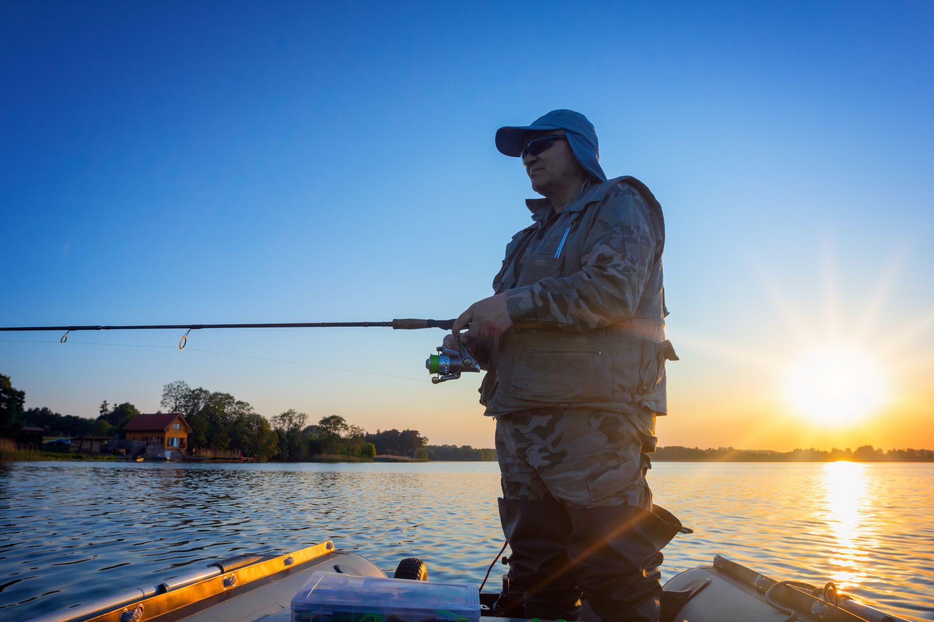 A man is fishing in a boat on a lake at sunset.