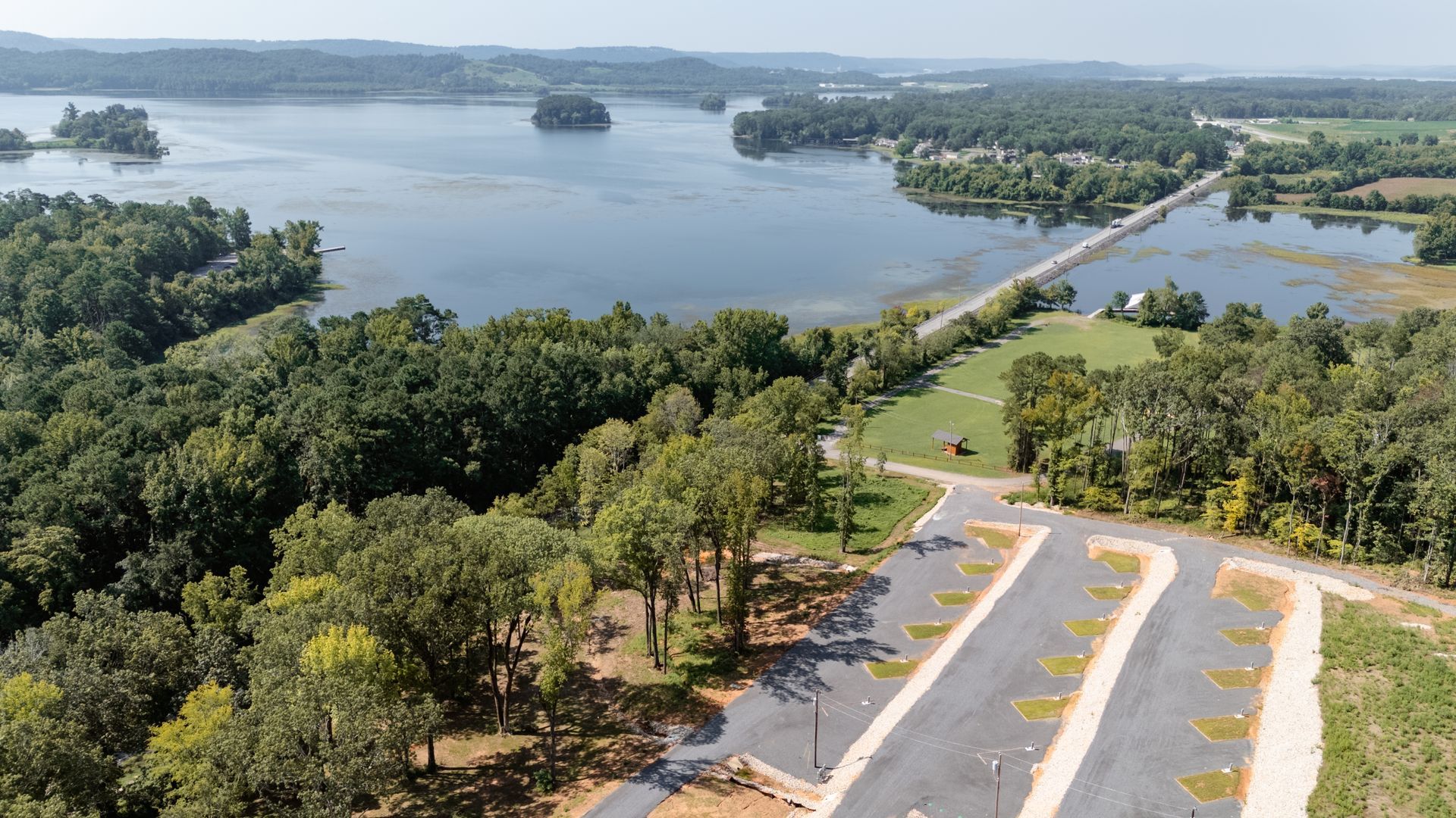 An aerial view of a lake surrounded by trees and a road.