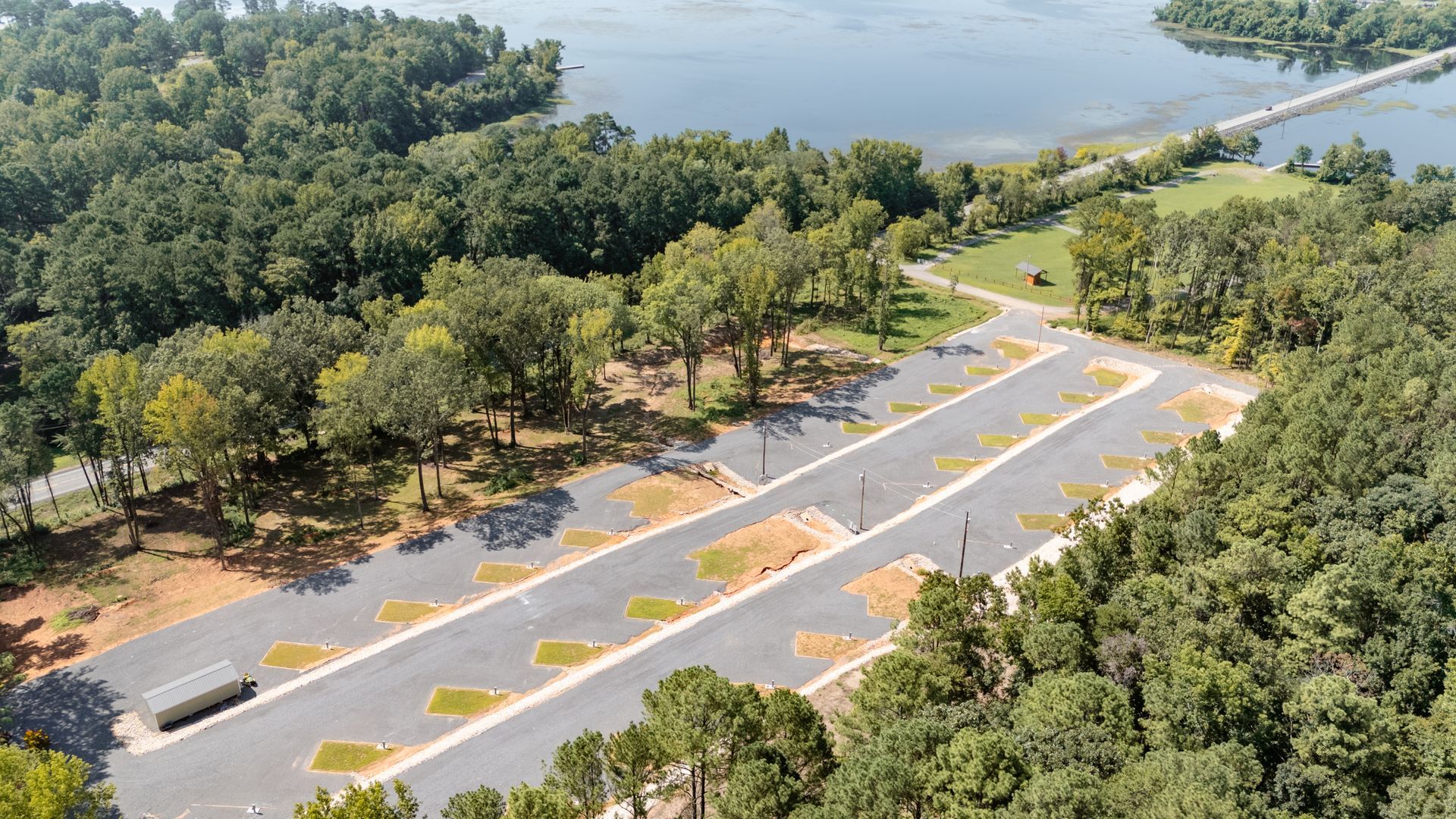 An aerial view of a road surrounded by trees next to a lake.
