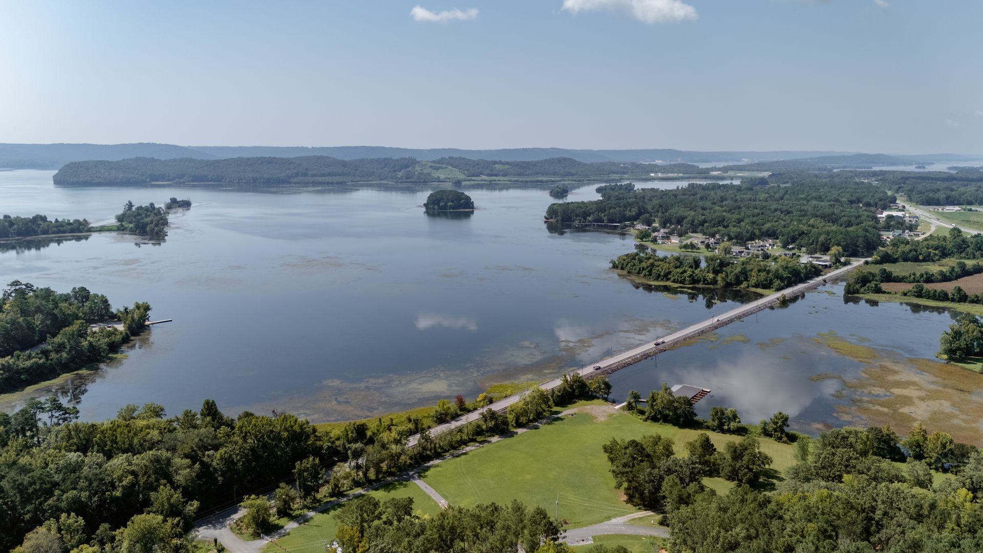 An aerial view of a large body of water surrounded by trees and a bridge.