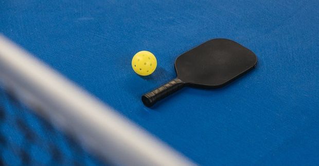 A paddle and a yellow ball are on a blue surface.