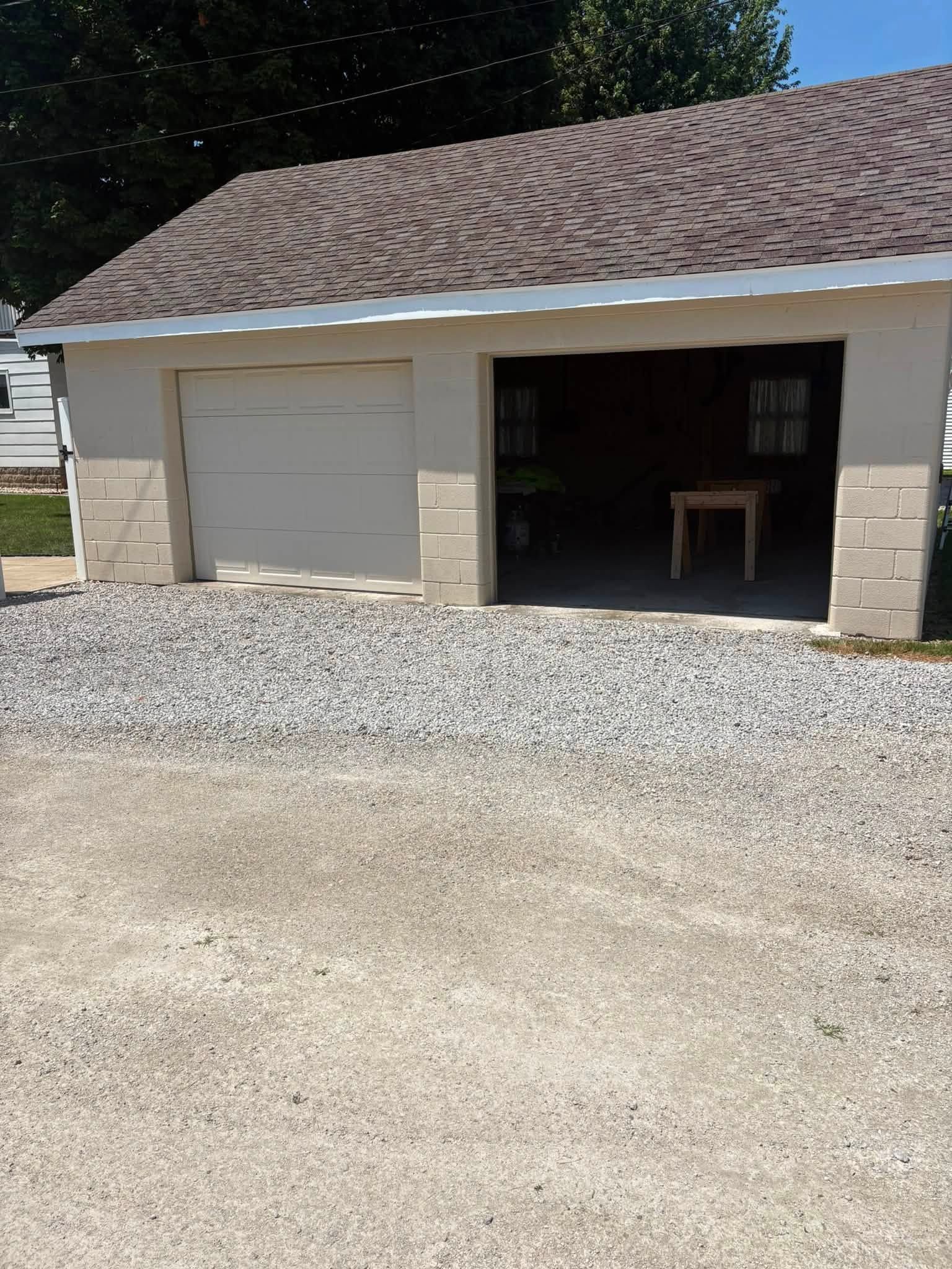 Small beige garage with white door and open bay, gravel driveway in front.
