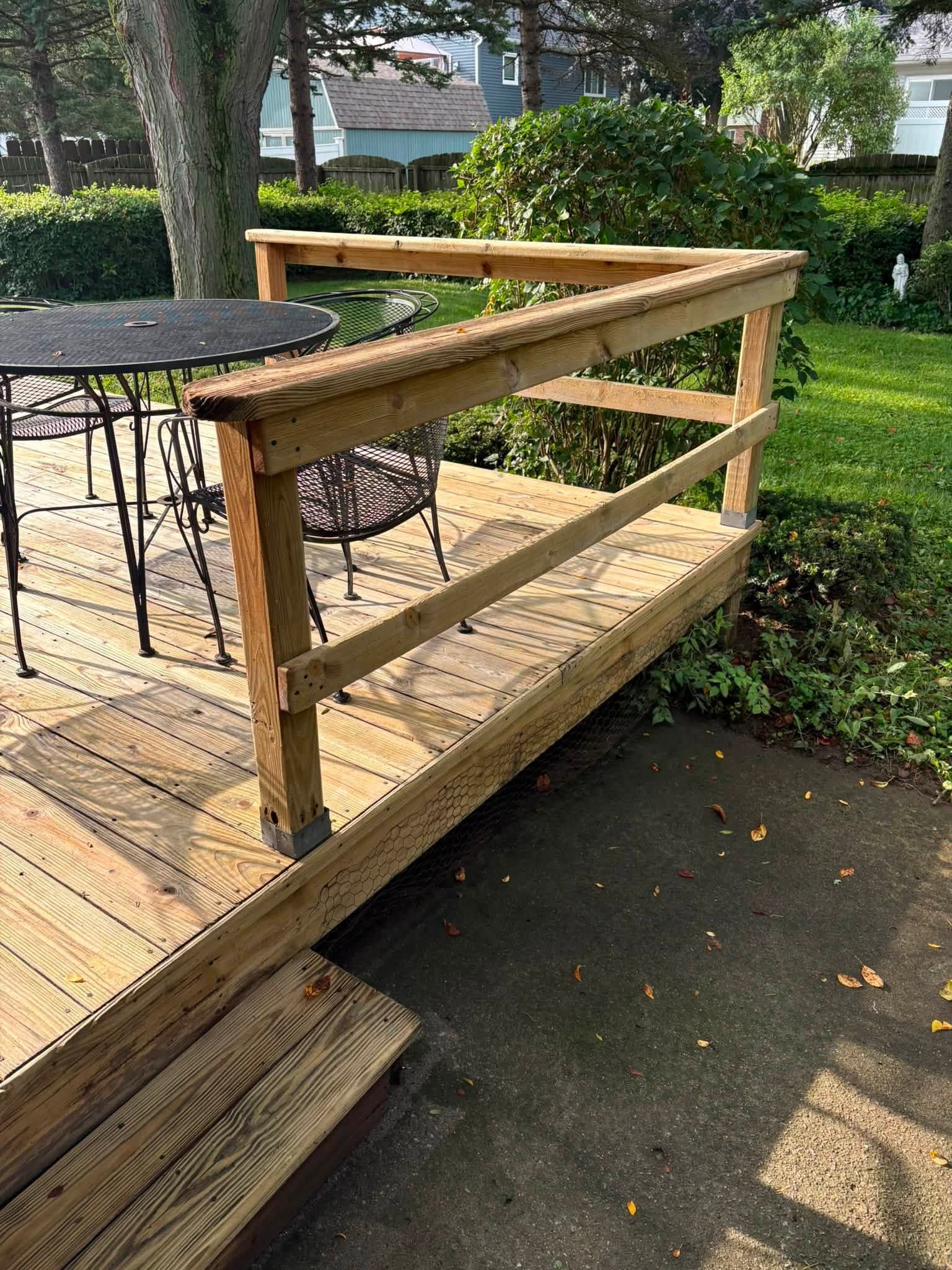 Wooden ramp with railings beside a patio and grassy yard, leading from deck to driveway.