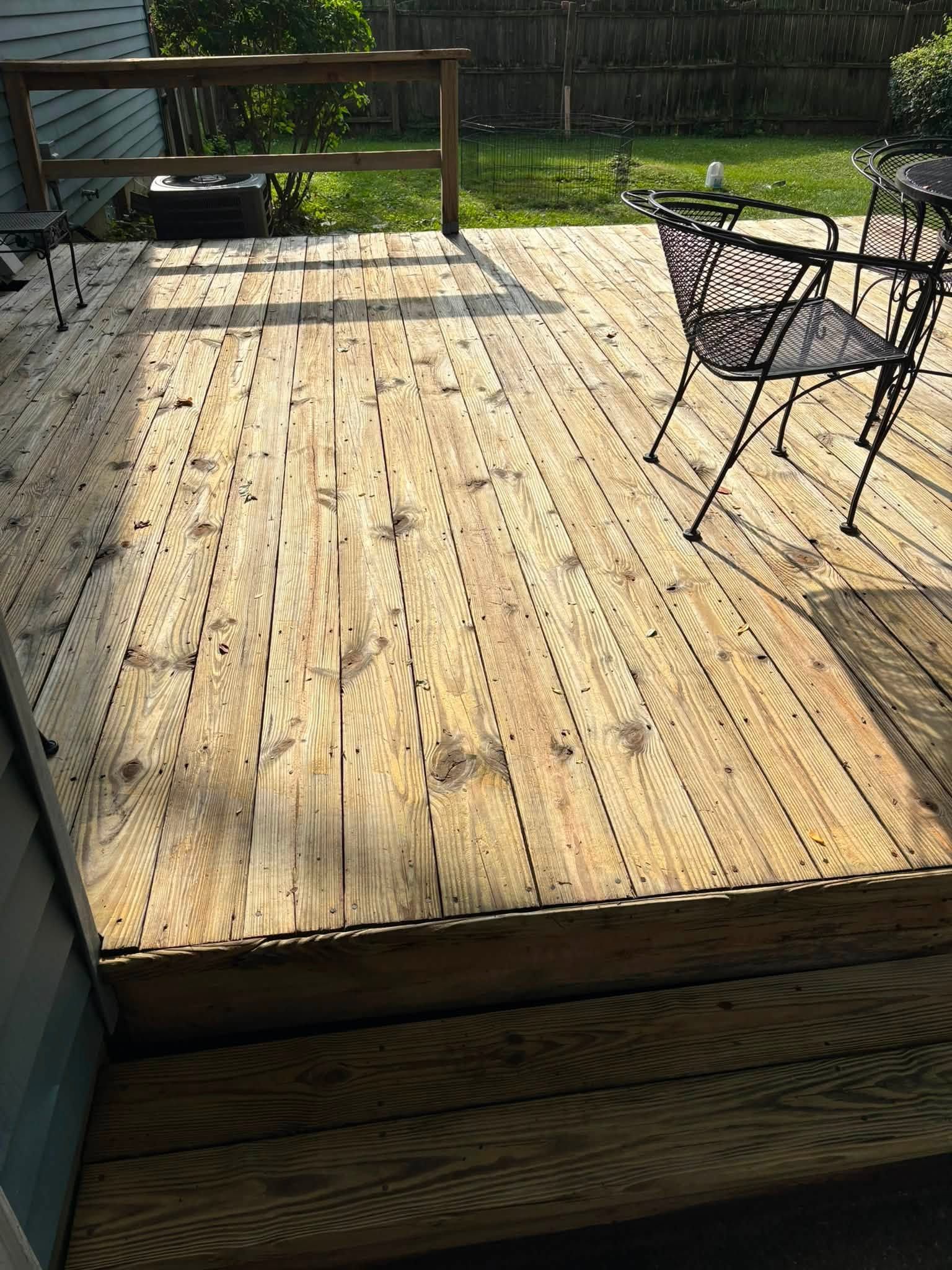 Weathered wooden backyard deck with a black metal chair and sunlight casting shadows
