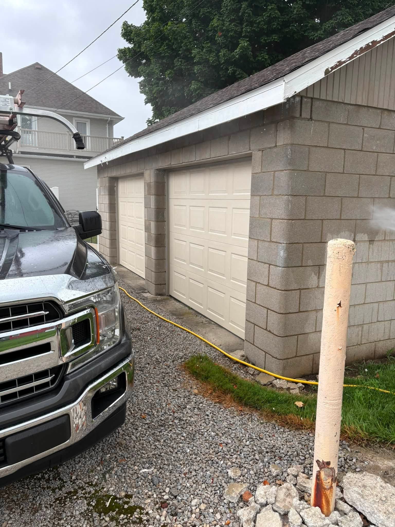 Gray garage beside a black truck on a gravel driveway, with a weathered white post in front.