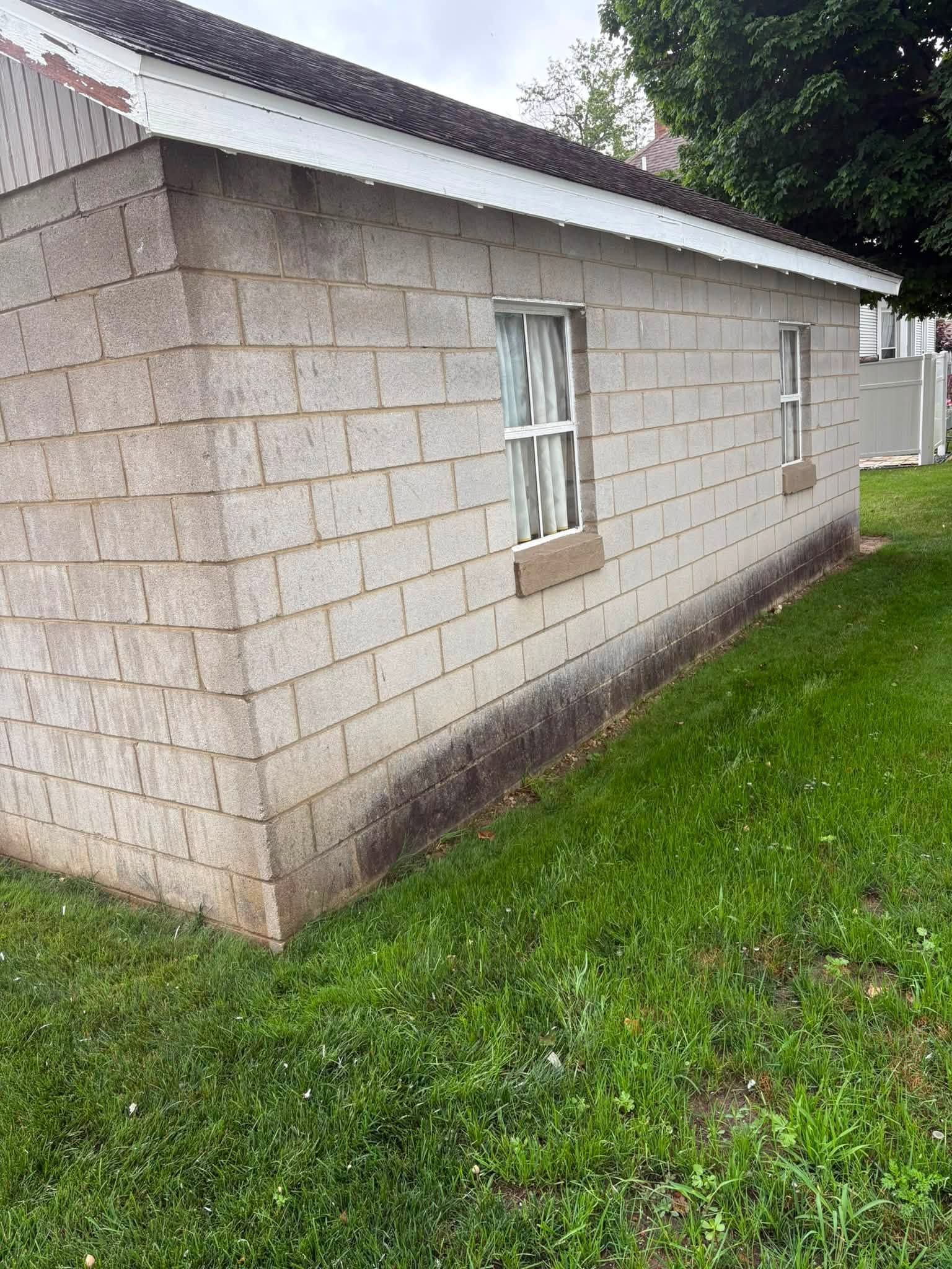 White cinderblock house exterior with a small window, metal roof, and green lawn beside it