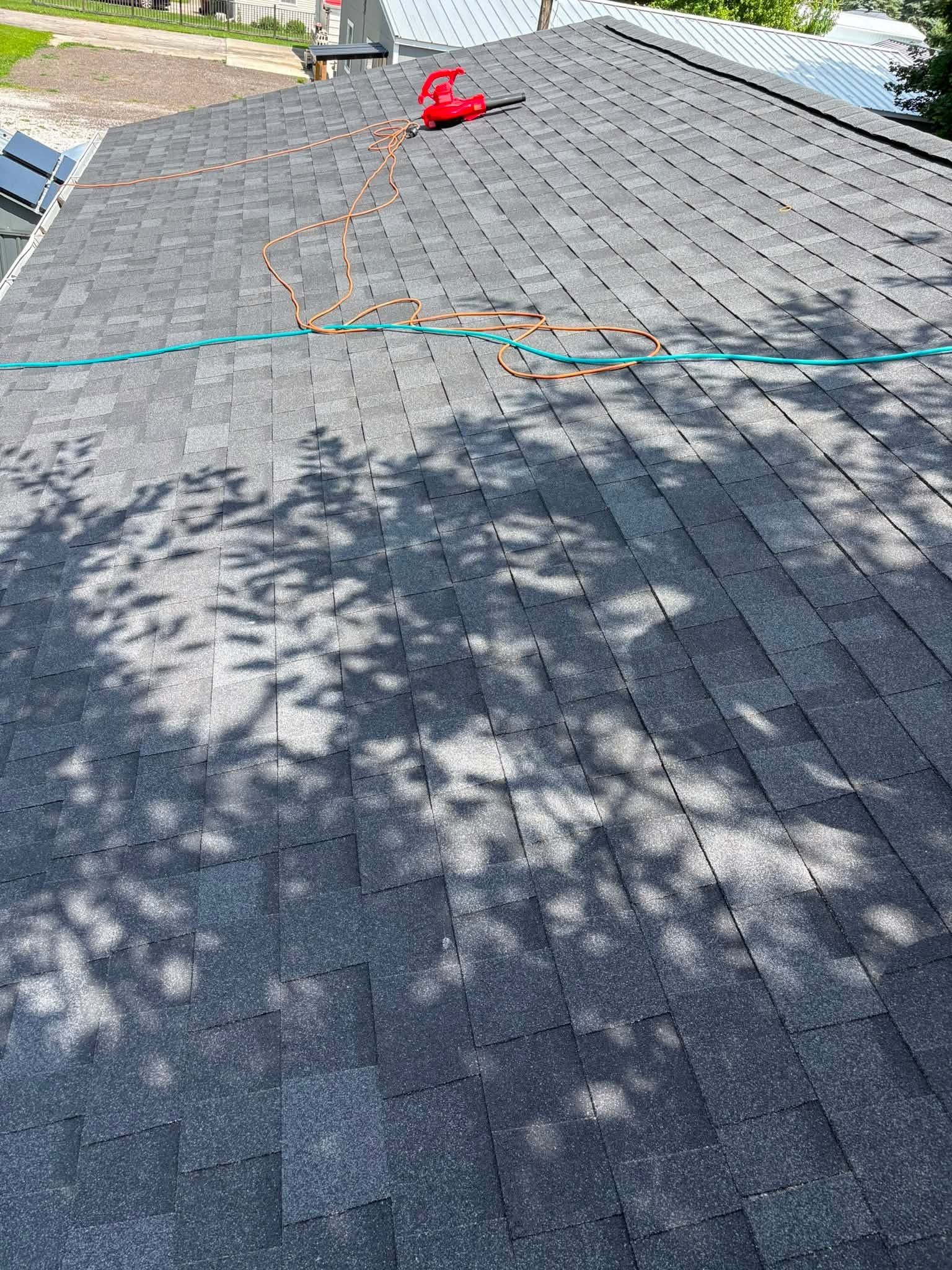 Gray shingled roof with a green hose and red tool near the ridge in sunlight