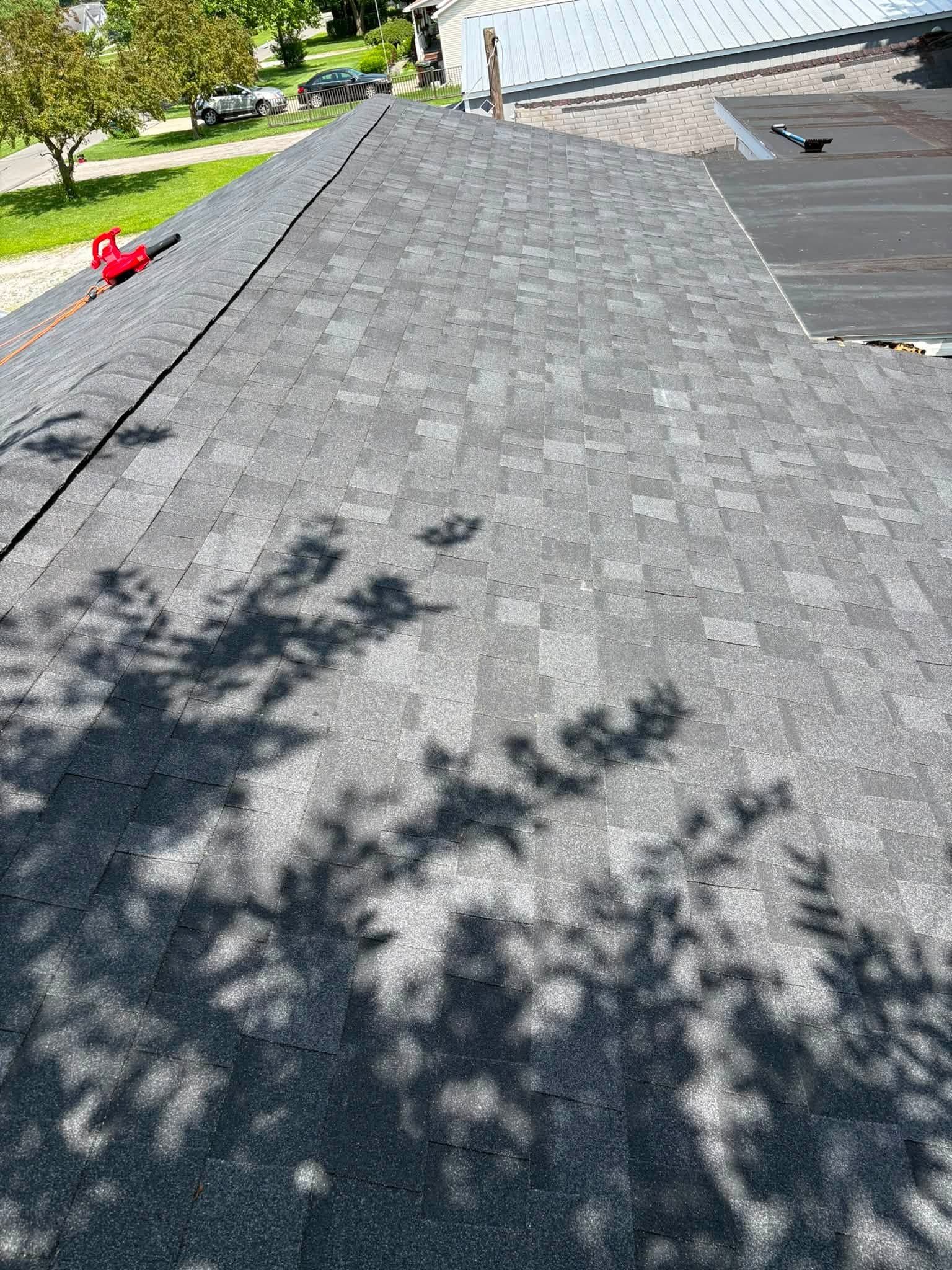 Shingled roof with a red vent and tree shadows beside a house and driveway