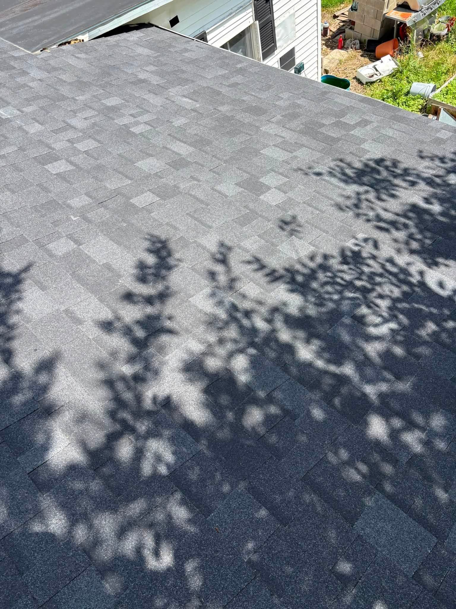 Shaded gray shingle rooftop with tree shadows and a white house edge in the background