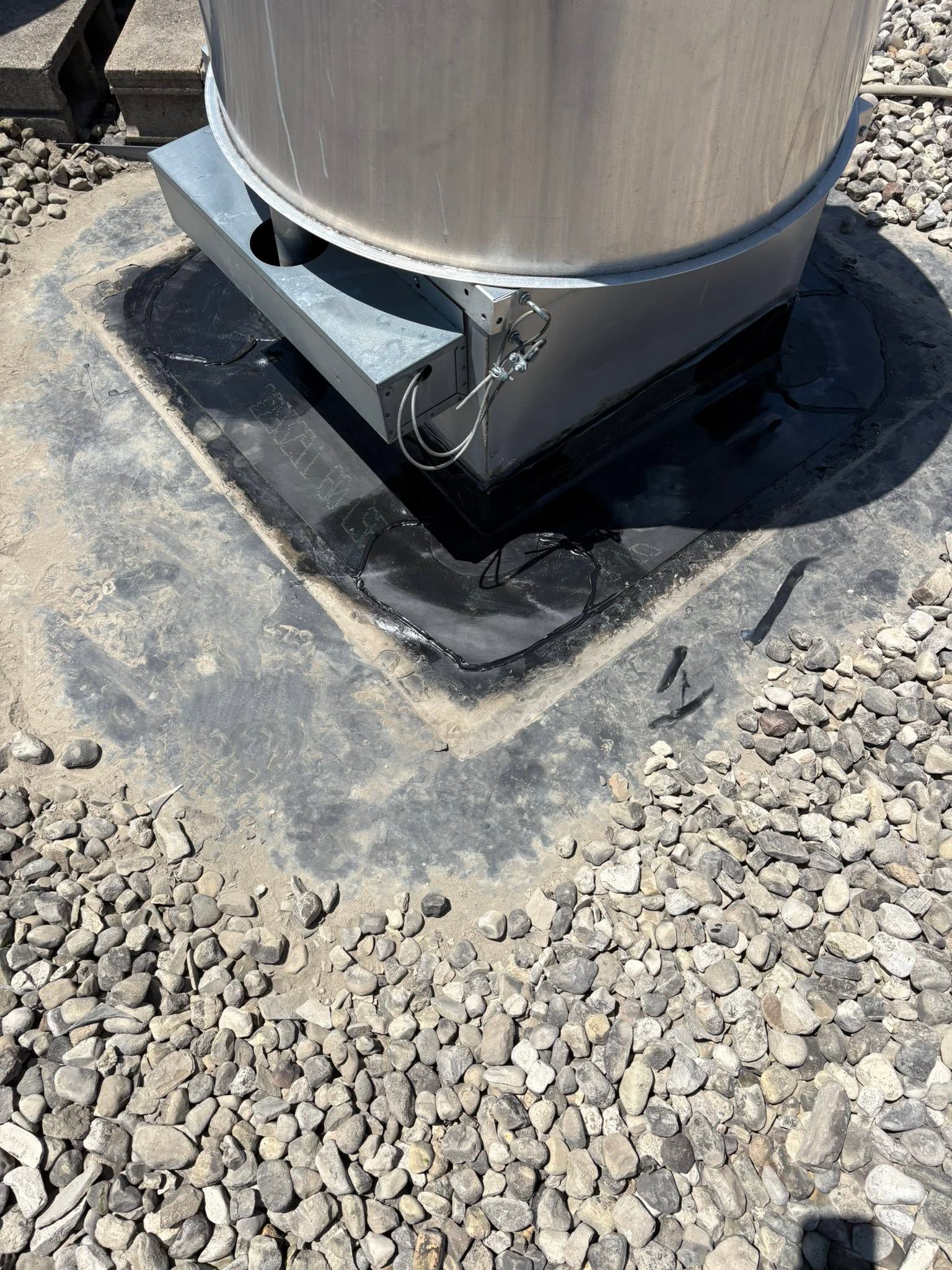 Metal tank base on a concrete pad surrounded by gravel, with staining and a small drain pipe.