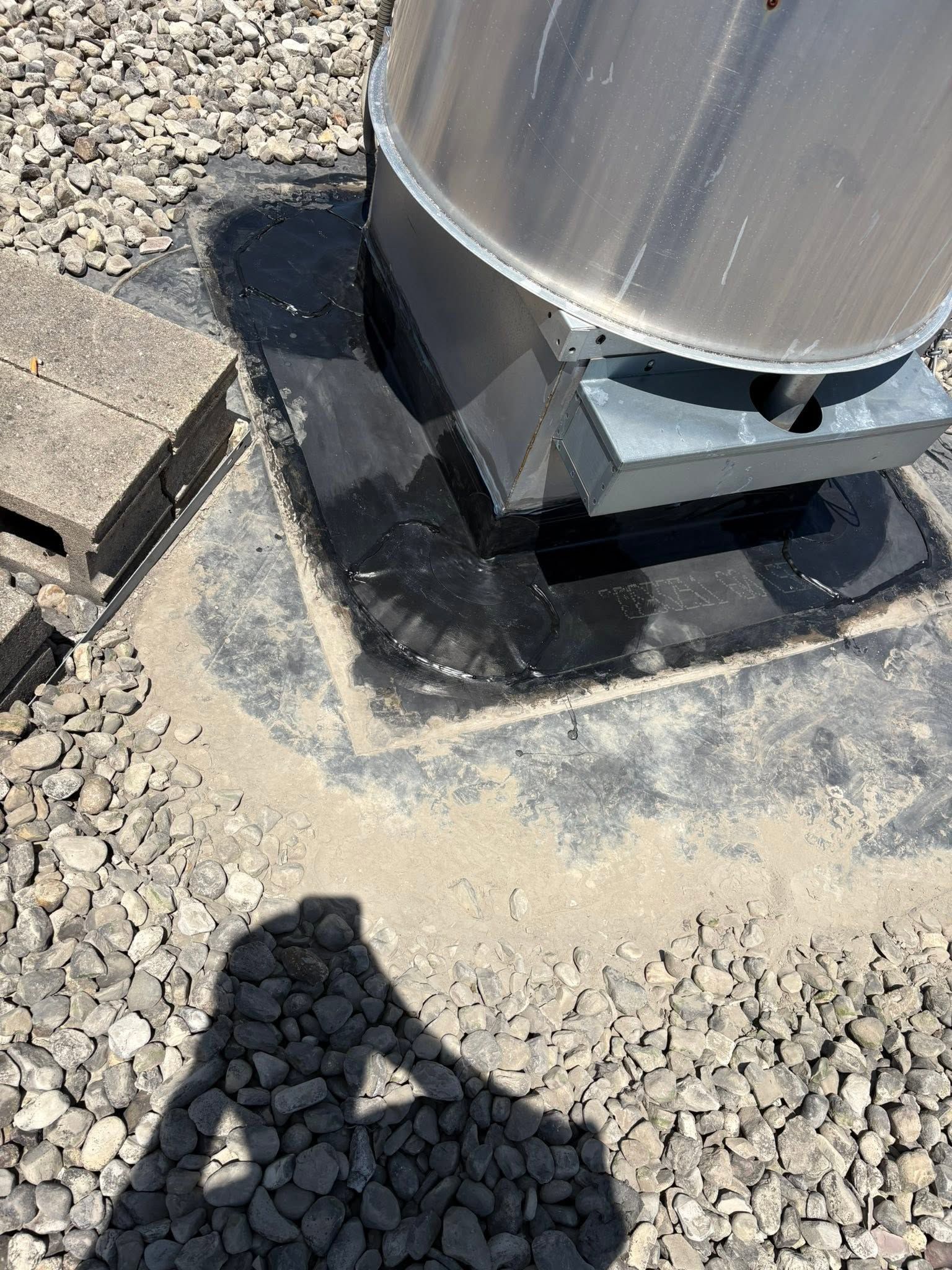 Large metal tank on a concrete pad, surrounded by gravel, with a person’s shadow in the foreground