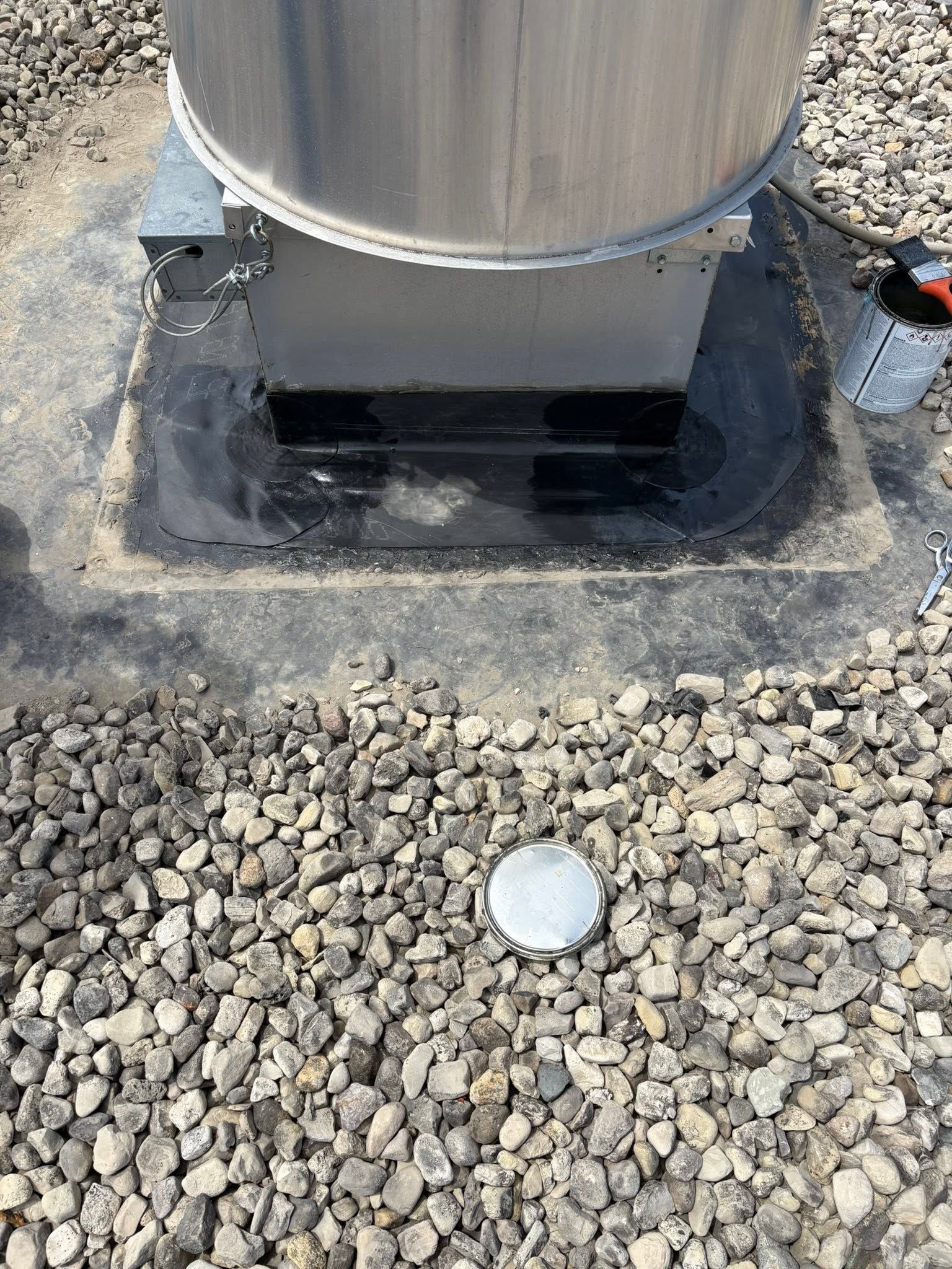 Metal utility pole base on gravel, with a white cap nearby.