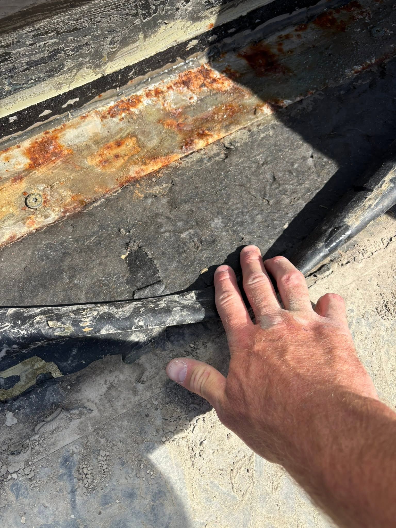 Hand inspecting cracked, rust-stained concrete near a dark seam or curb edge.