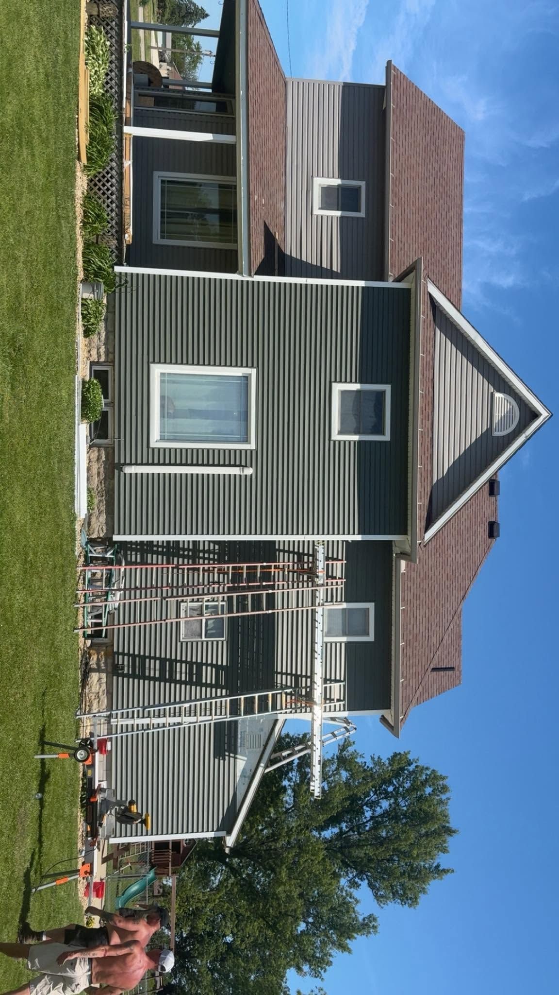 Green and gray house with red roof, front porch, and a fenced yard under a blue sky